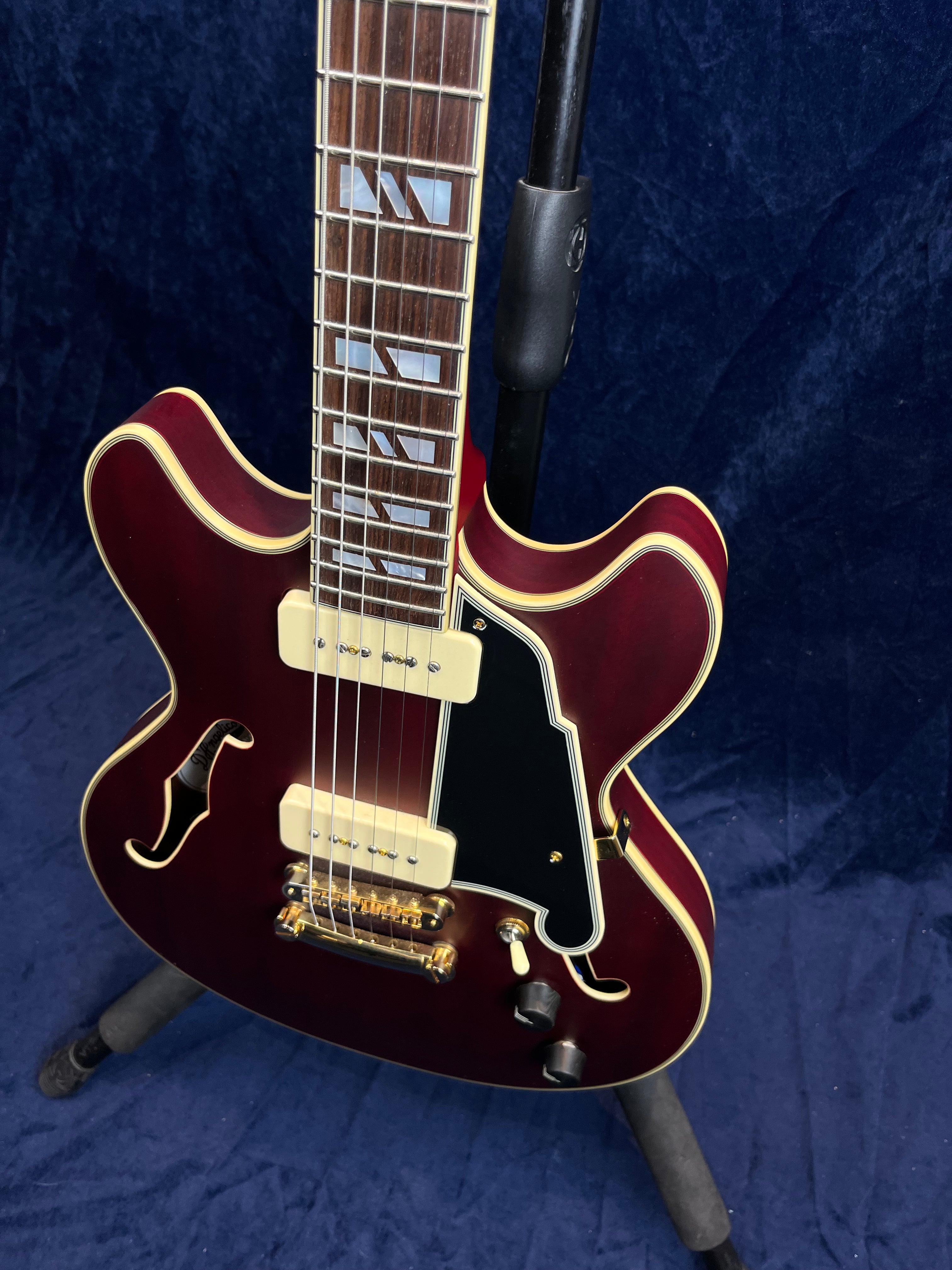 Cherry red semi-hollow electric guitar with cream binding, two cream pickups, gold bridge, black pickguard, and decorative fretboard inlays.