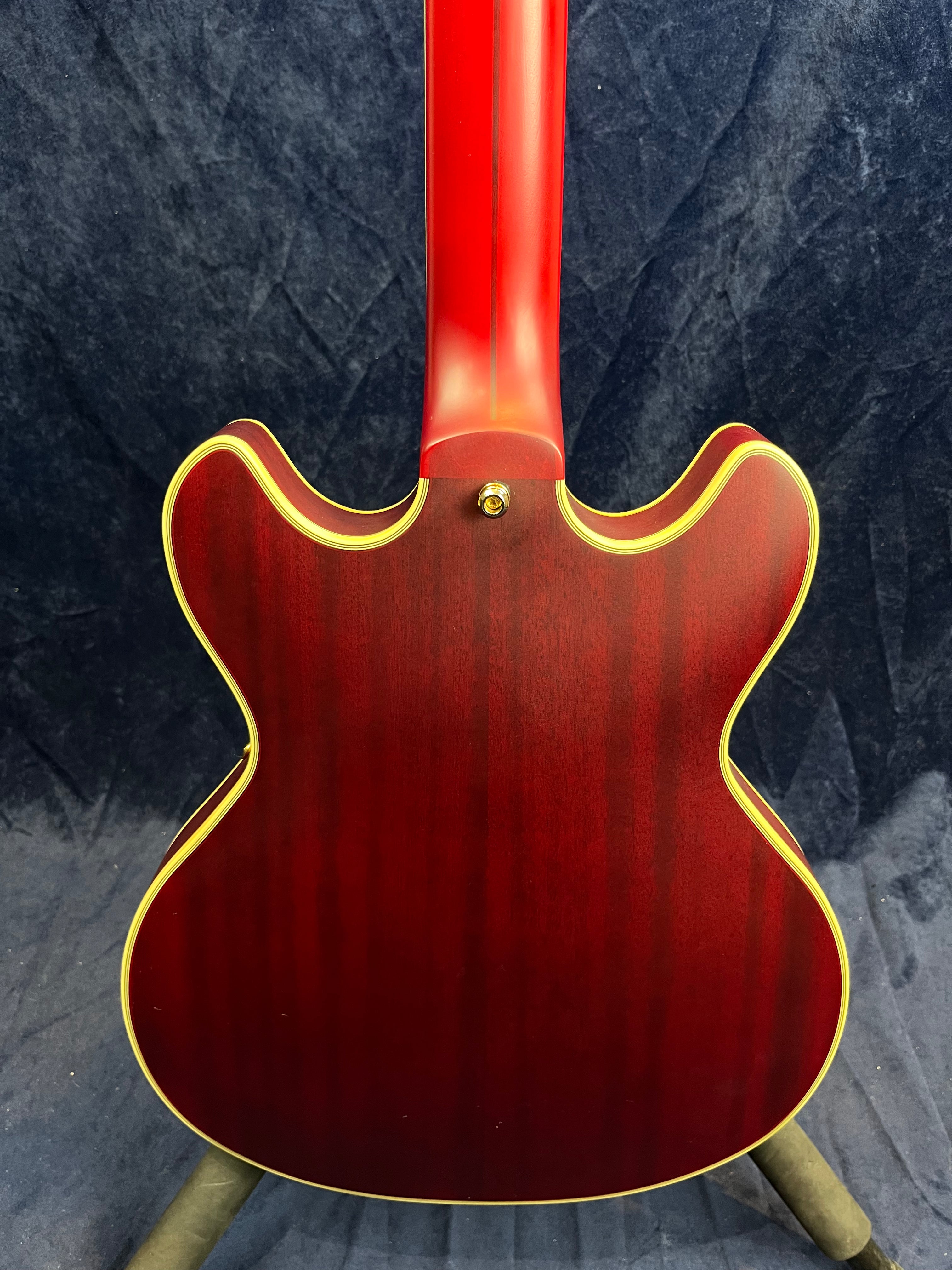 Back view of a cherry red semi-hollow electric guitar with a double cutaway shape and yellow binding along the edges.
