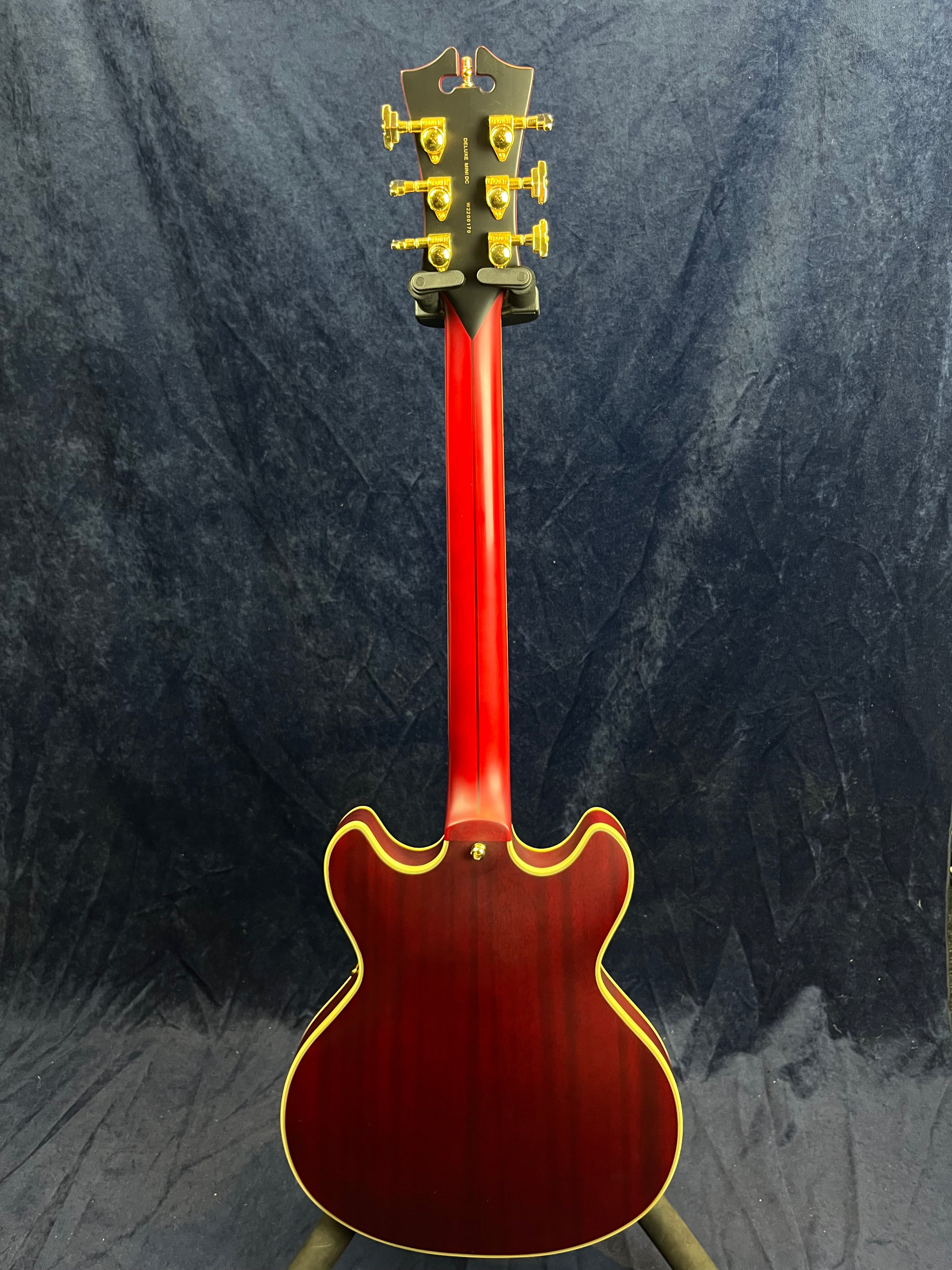 Red semi-hollow electric guitar shown from the back, with gold tuning pegs and cream binding around the body and neck.