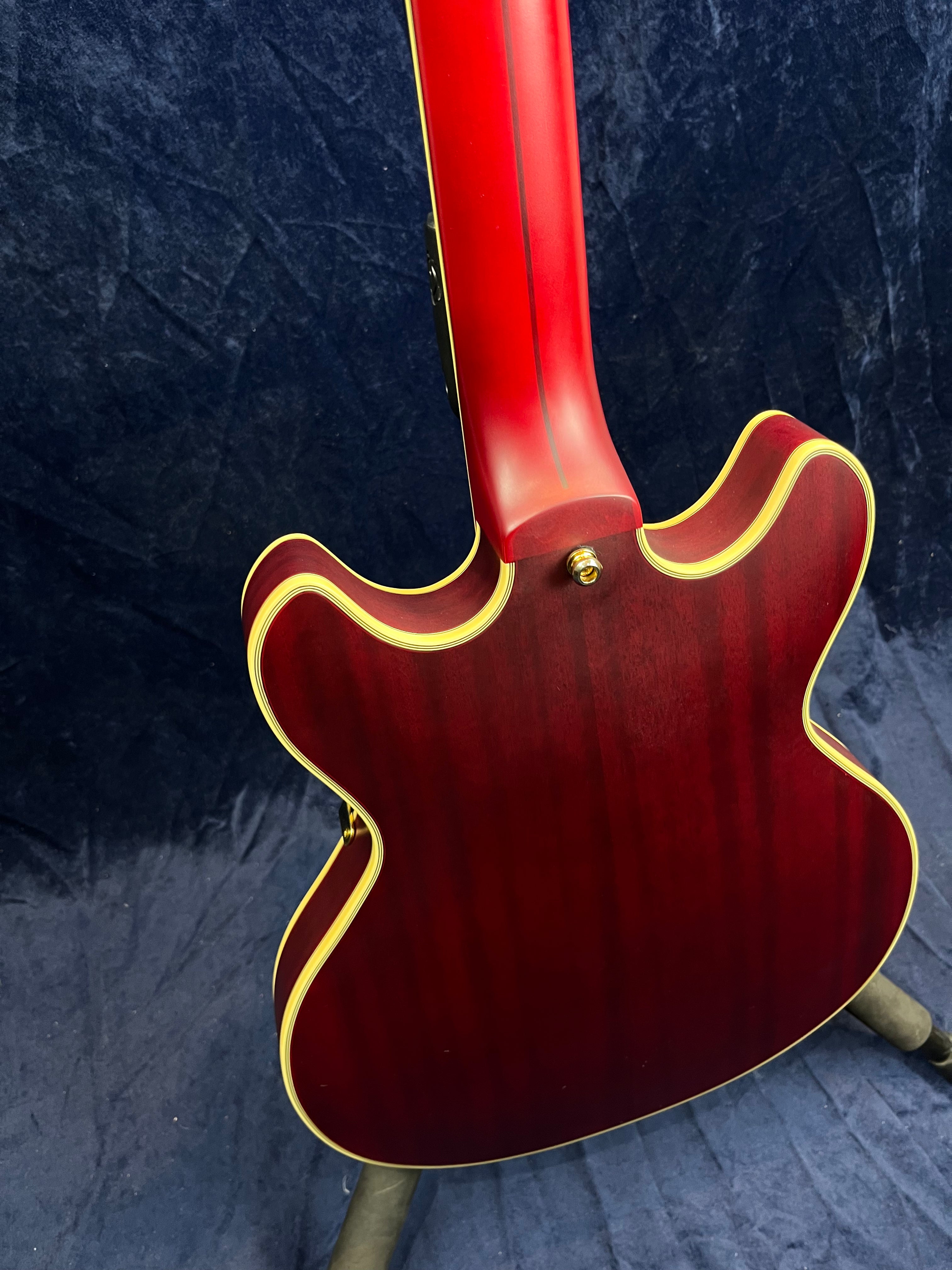 Cherry red electric guitar viewed from the back, showing curved double-cutaway body and cream binding along the edges and neck.