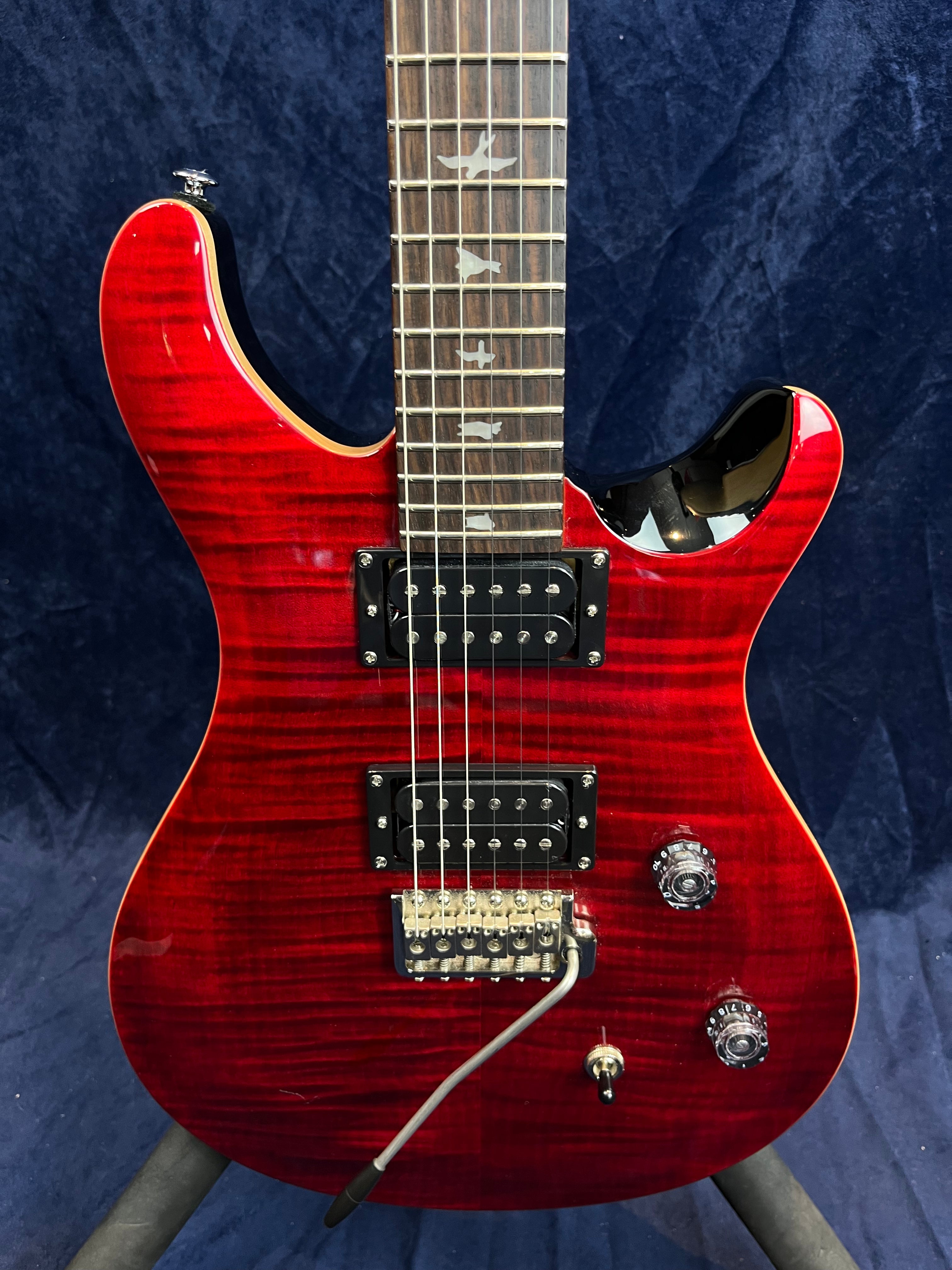 Guitare électrique rouge brillant avec deux micros humbuckers noirs, vibrato argenté, deux boutons de réglage et repères en forme d’oiseaux sur le manche.
