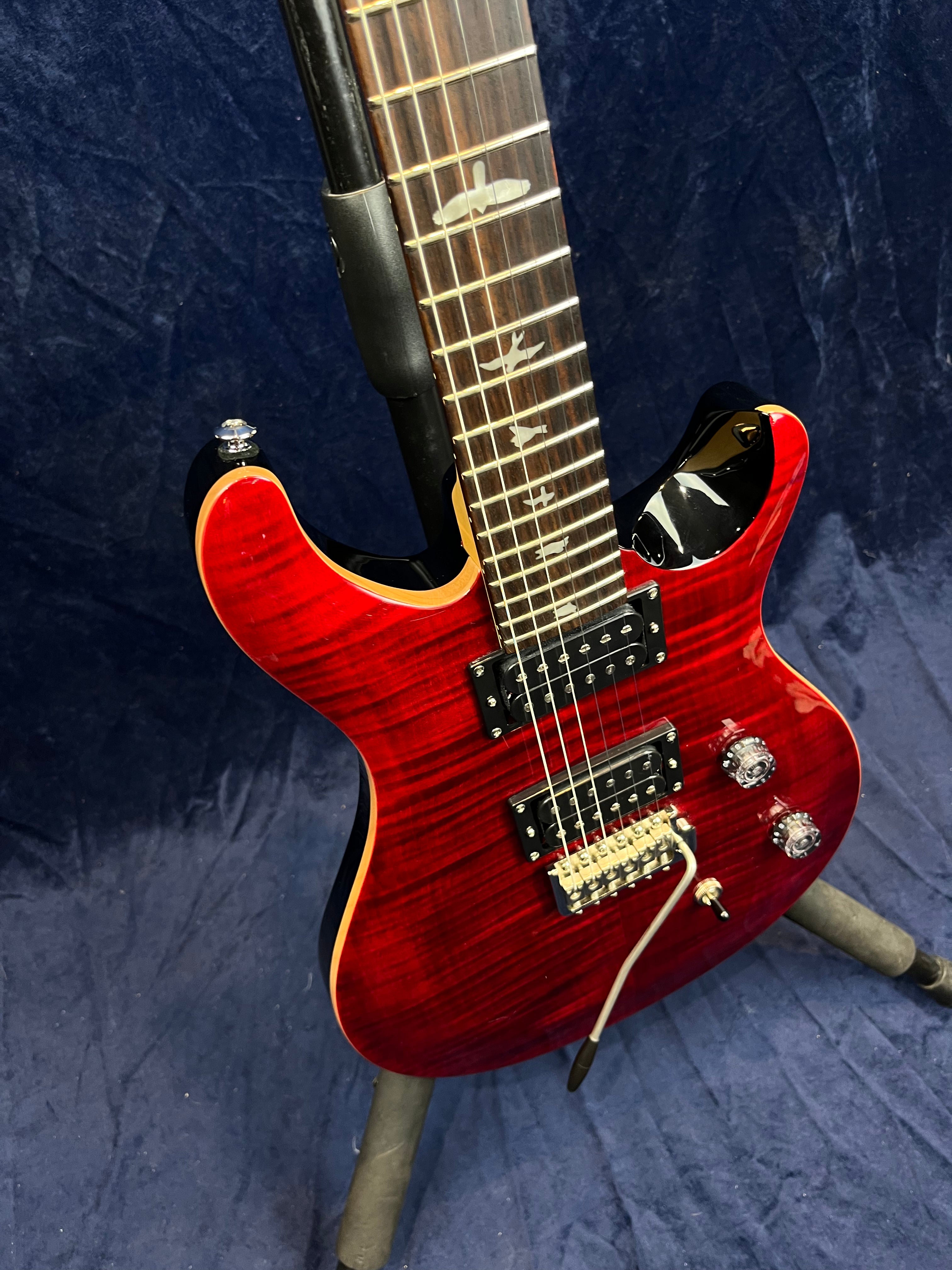 Guitare électrique rouge brillant avec deux micros humbucker, trois boutons de réglage, vibrato et repères en forme d’oiseaux sur le manche.