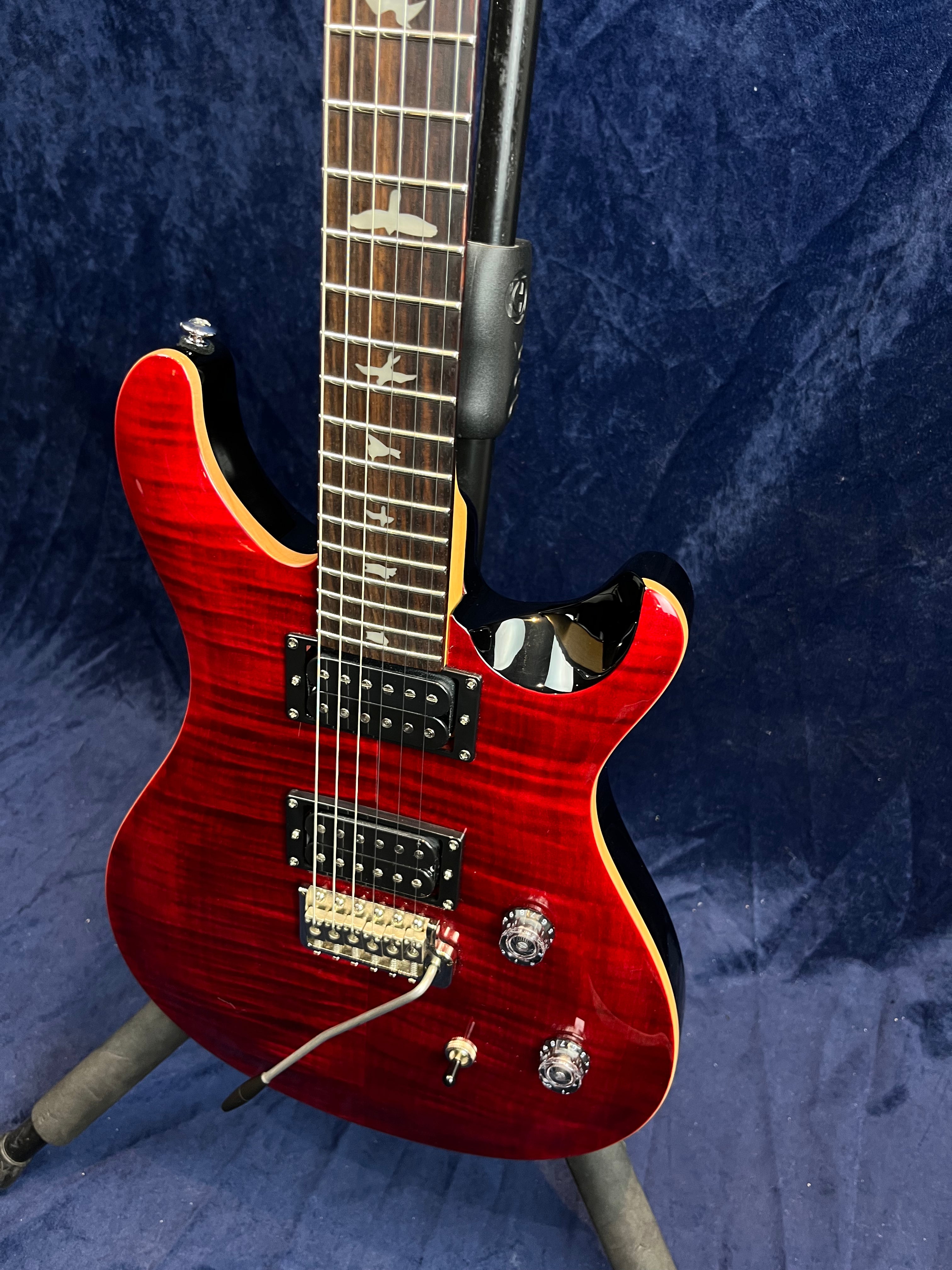 Guitare électrique rouge à deux micros doubles, touche ornée d’incrustations en forme d’oiseaux, équipée d’un vibrato et de deux boutons de réglage.