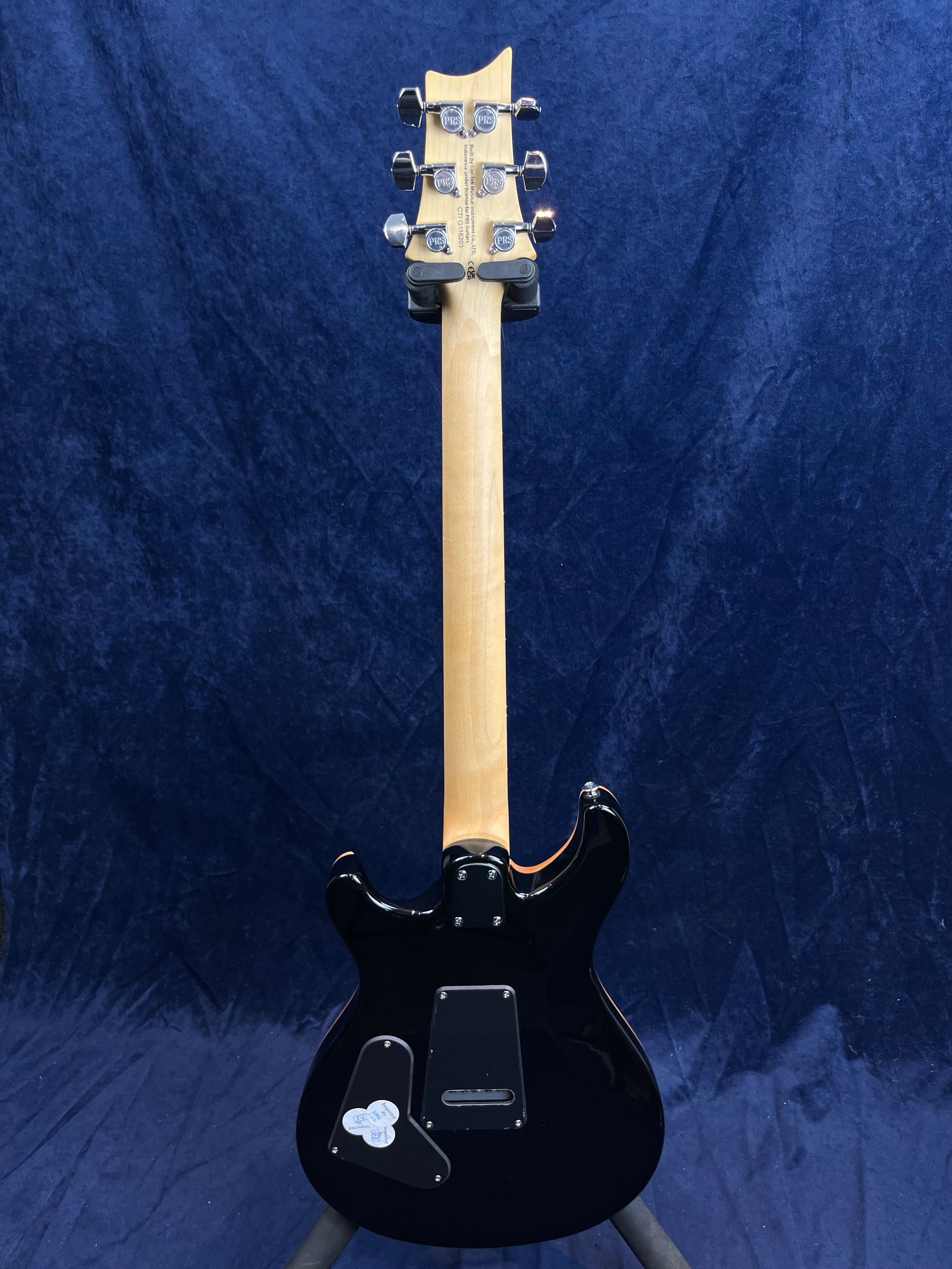 Guitare électrique noire vue de dos, manche en bois clair, six mécaniques argentées, deux plaques de protection noires fixées à l’arrière du corps.