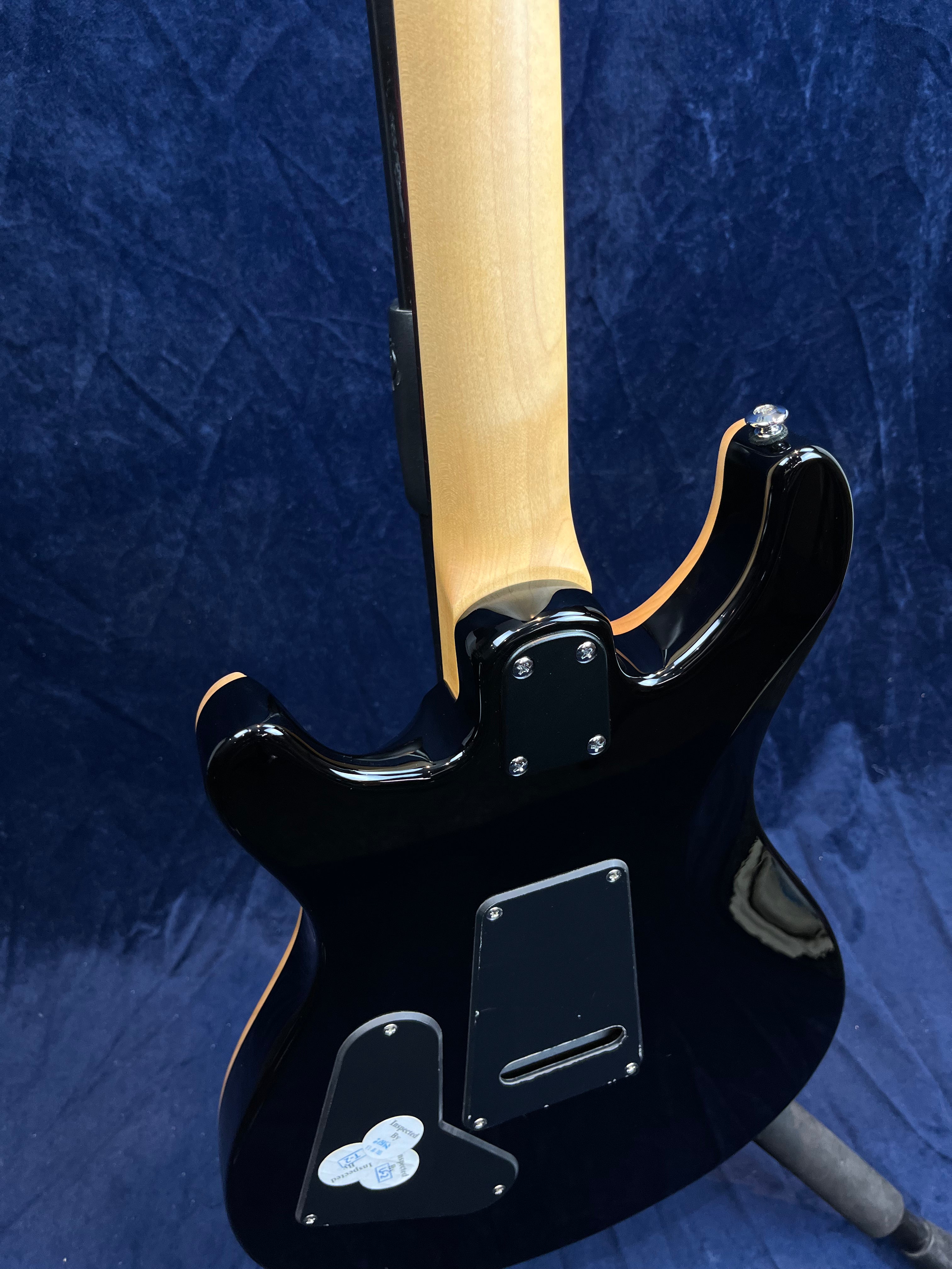 Guitare électrique noire vue de dos, manche en bois clair, plaques de protection noires fixées par des vis sur le corps.