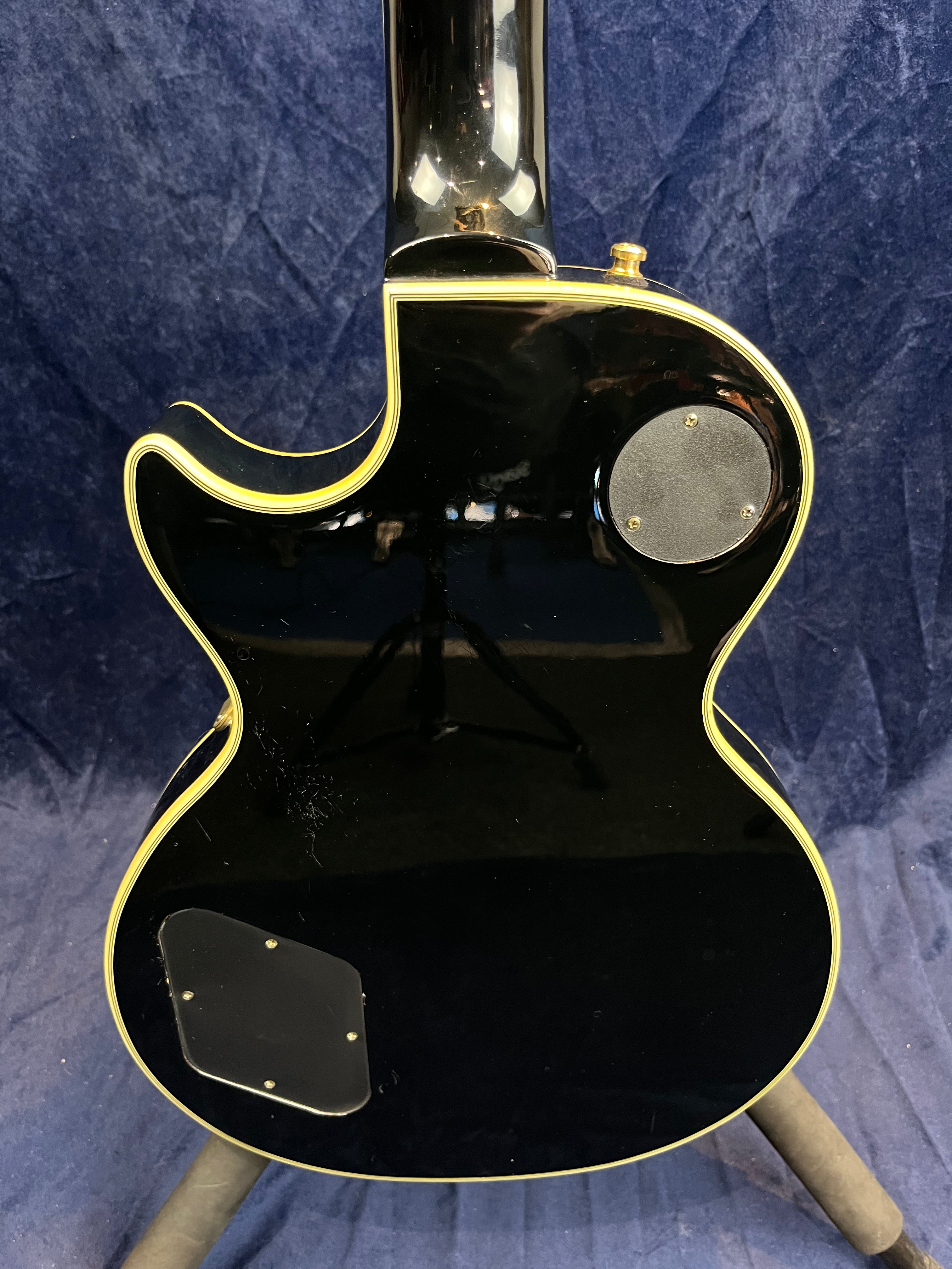 Black electric guitar back with cream binding, two round plastic access covers, and a single cutaway on the left side.
