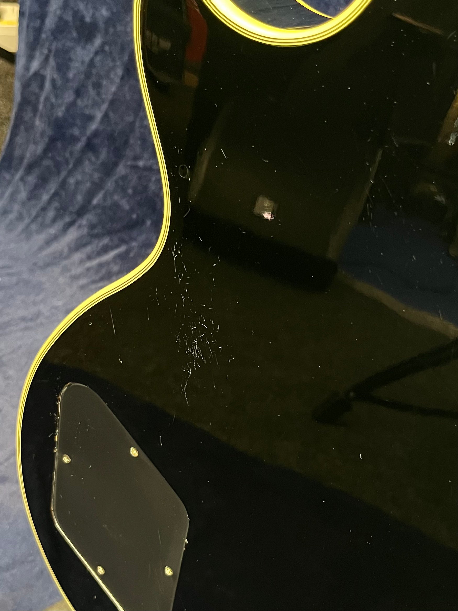 Glossy black electric guitar body with yellow trim, visible surface scratches, and a black backplate secured with screws.