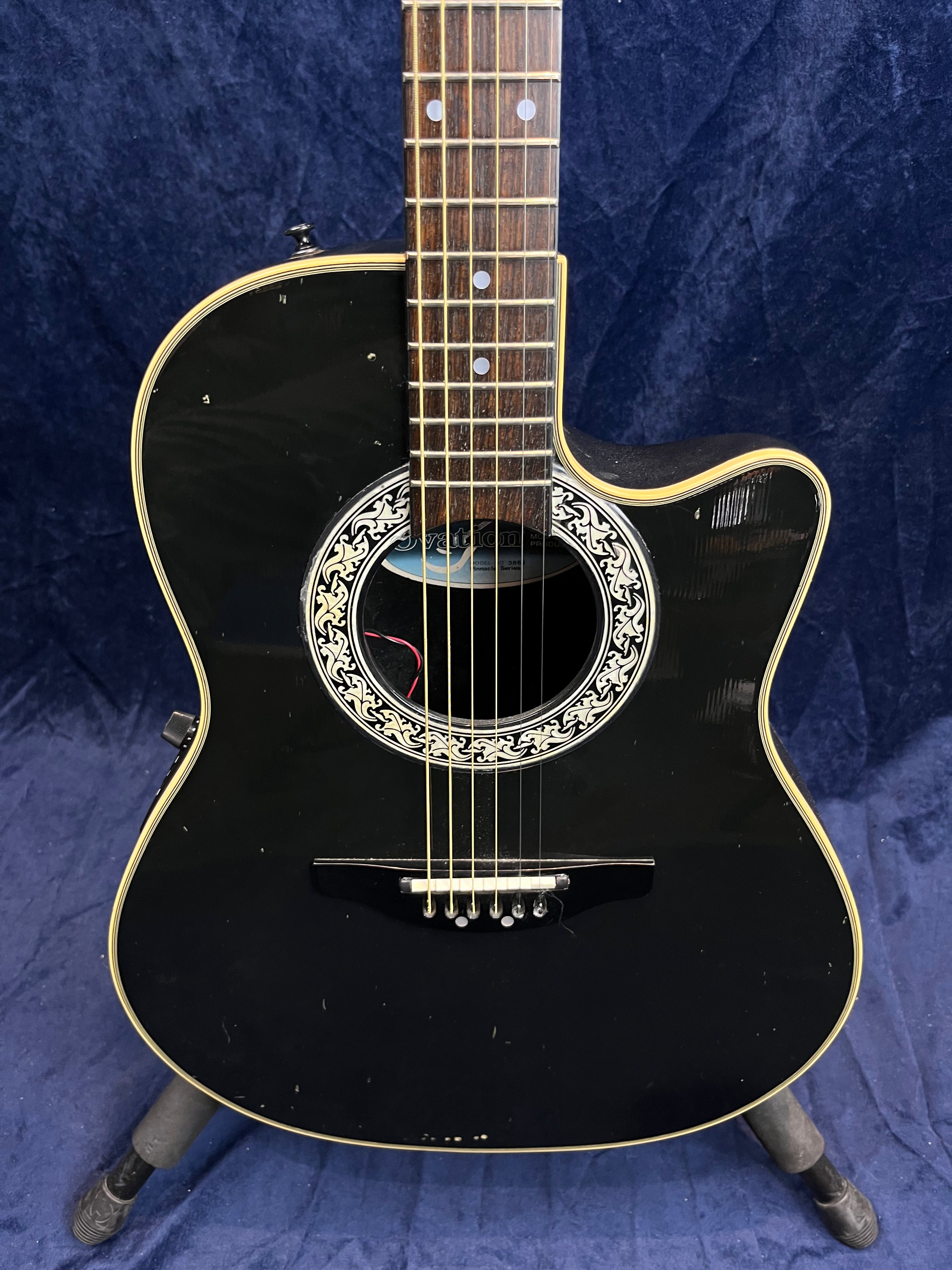 Black acoustic guitar with a cutaway body, ornate white and black rosette, cream binding, and visible minor scuffs on the front.