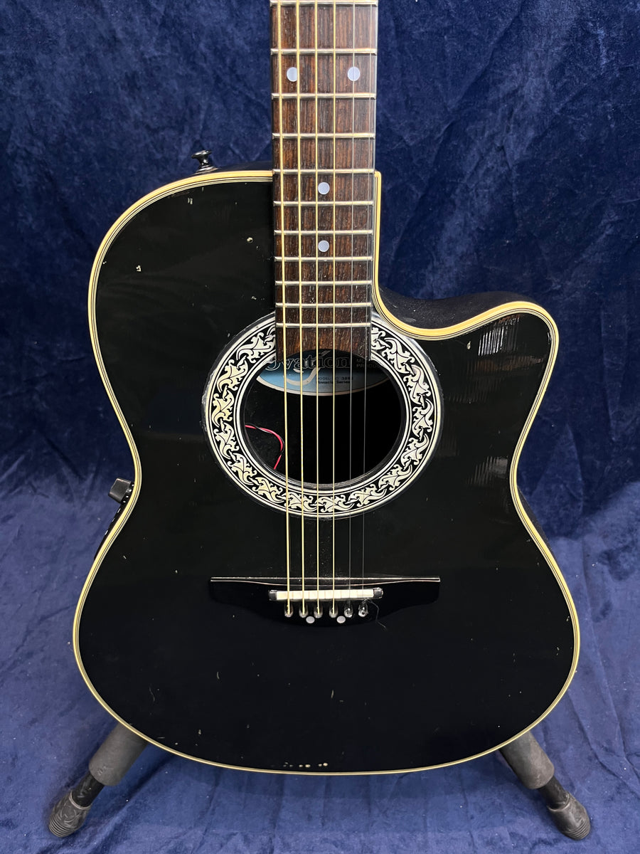 Black acoustic guitar with a cutaway body, ornate white and black rosette, cream binding, and visible minor scuffs on the front.
