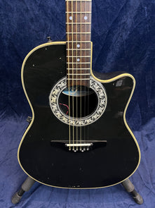 Black acoustic guitar with a cutaway body, ornate white and black rosette, cream binding, and visible minor scuffs on the front.