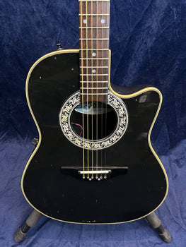 Black acoustic guitar with a cutaway body, ornate white and black rosette, cream binding, and visible minor scuffs on the front.