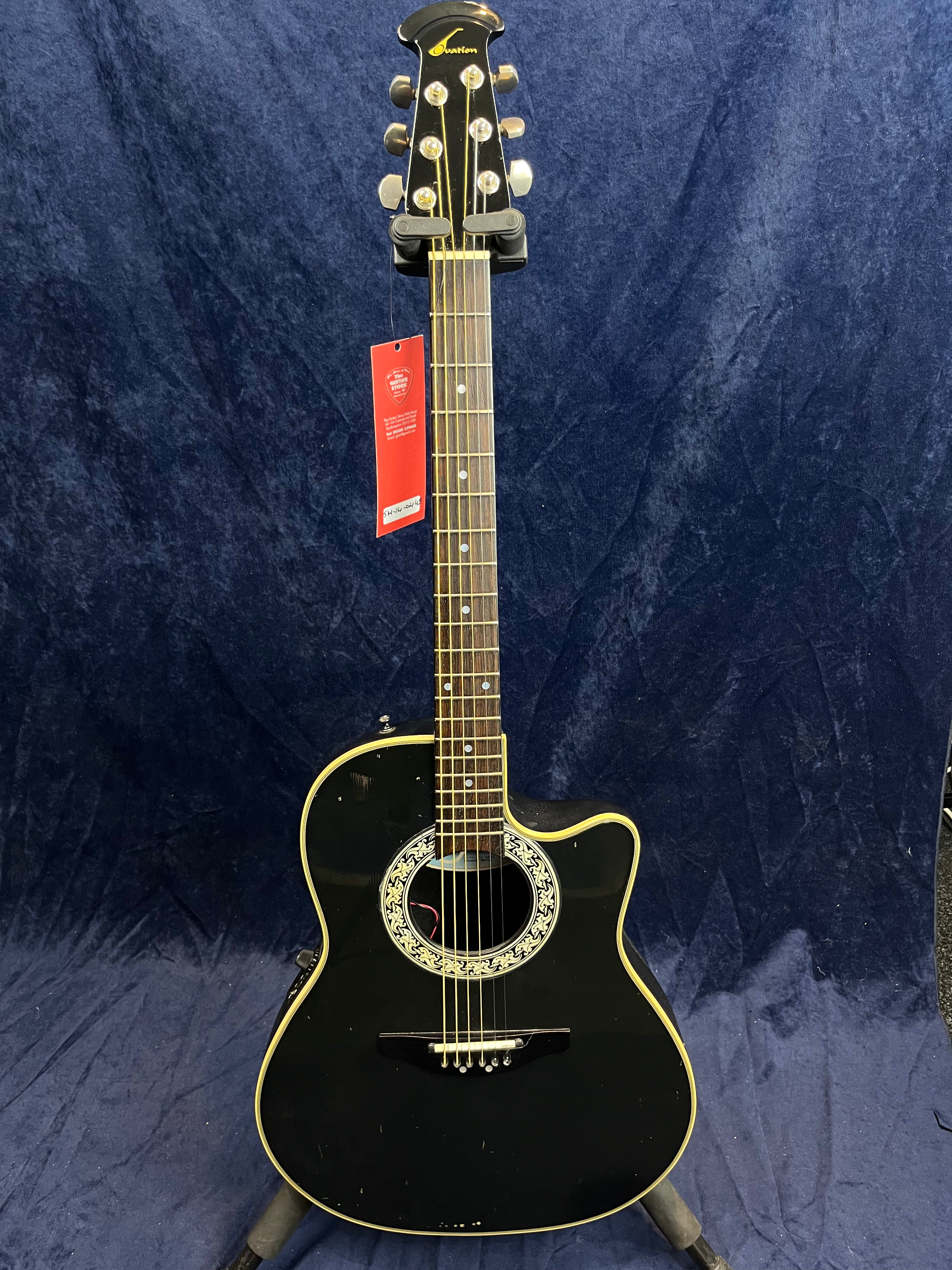 Black acoustic guitar with an ornate circular rosette, cutaway body, six strings, and gold tuning pegs on a dark background.