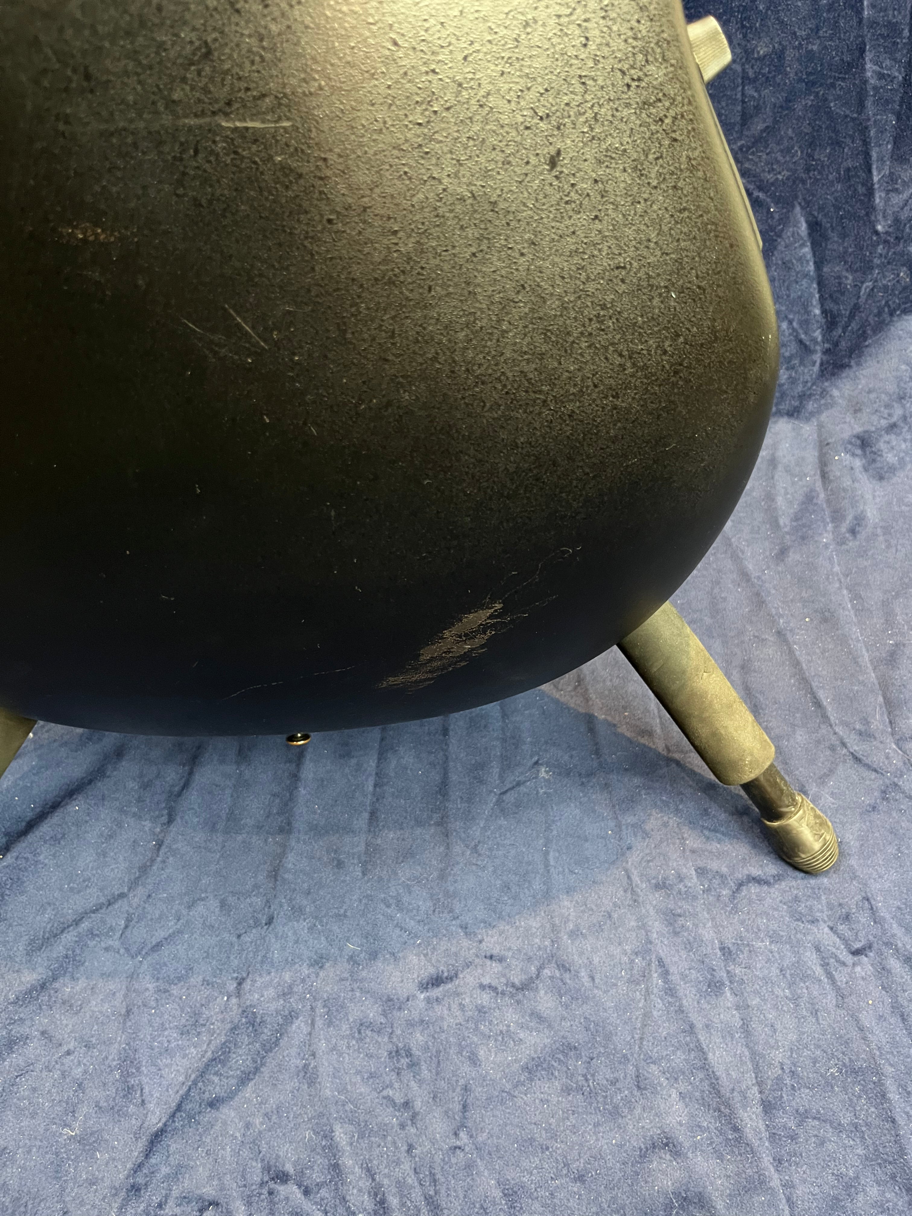 Back of a black acoustic guitar with visible scratches and scuff marks, resting on a stand over a blue fabric surface.