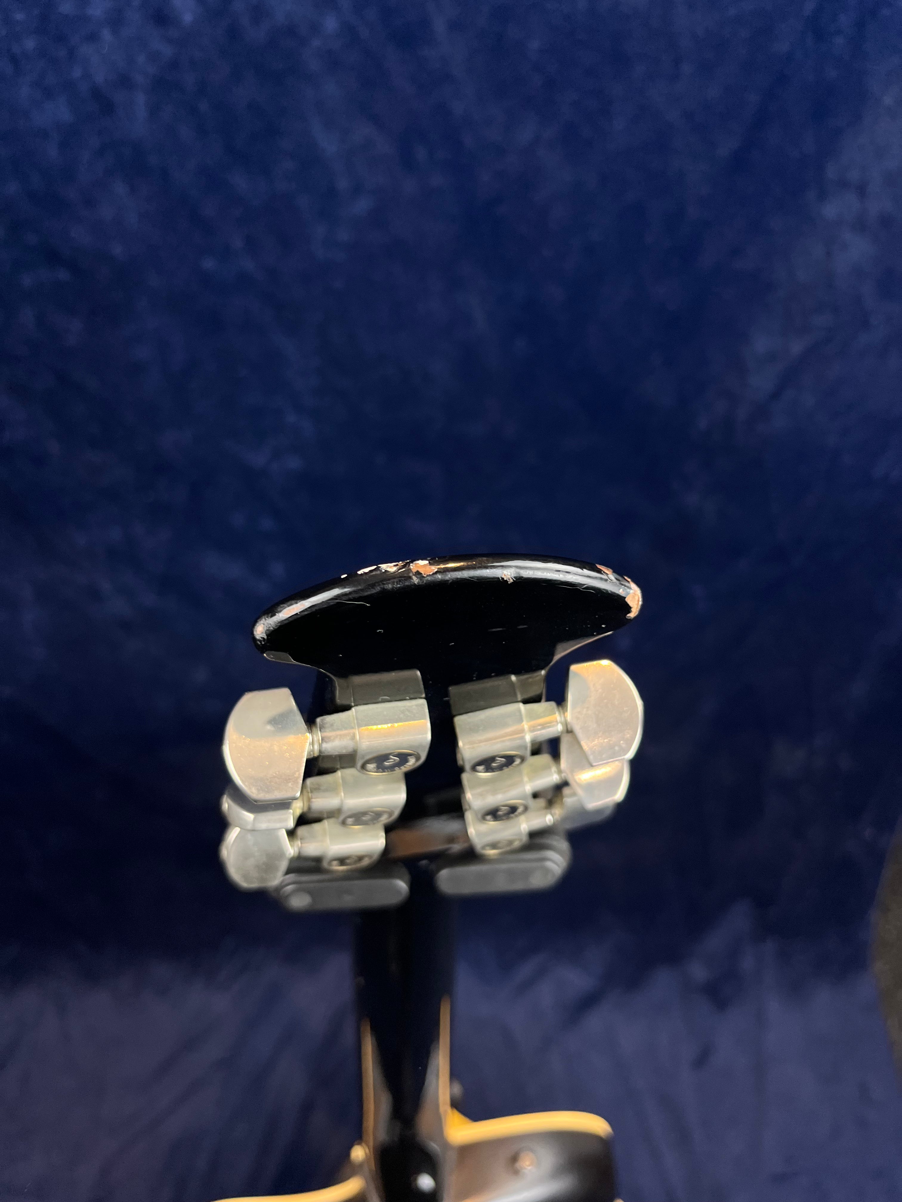 Close-up of an acoustic guitar headstock with metal tuning pegs and visible chips and wear on the top edge of the headstock.