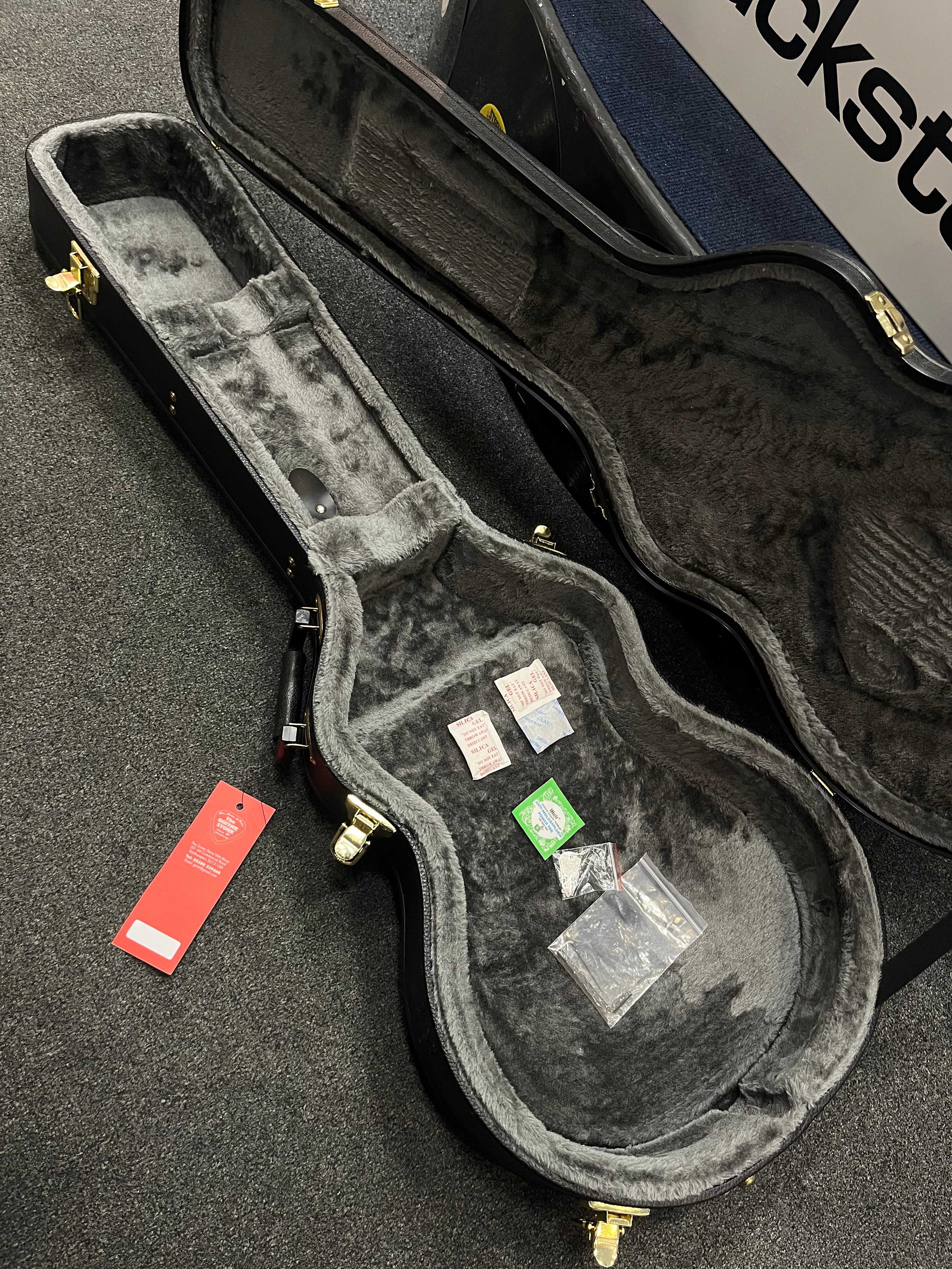 Empty plush-lined electric guitar case open on the floor, containing silica gel packets, a green label packet, and small ziplock bags.