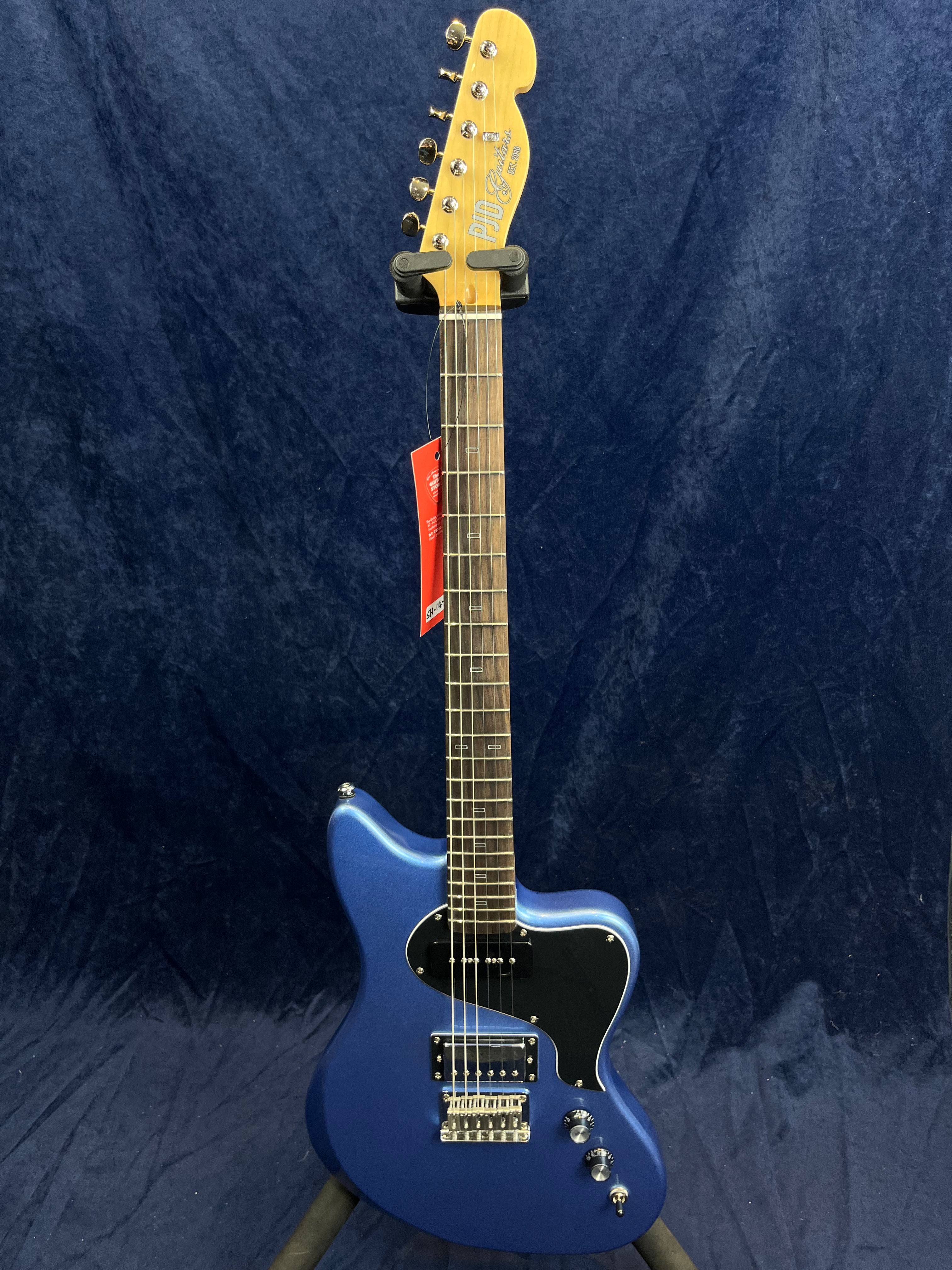 Metallic blue electric guitar with a black pickguard, two humbucker pickups, chrome hardware, and a maple headstock, displayed upright on a stand.