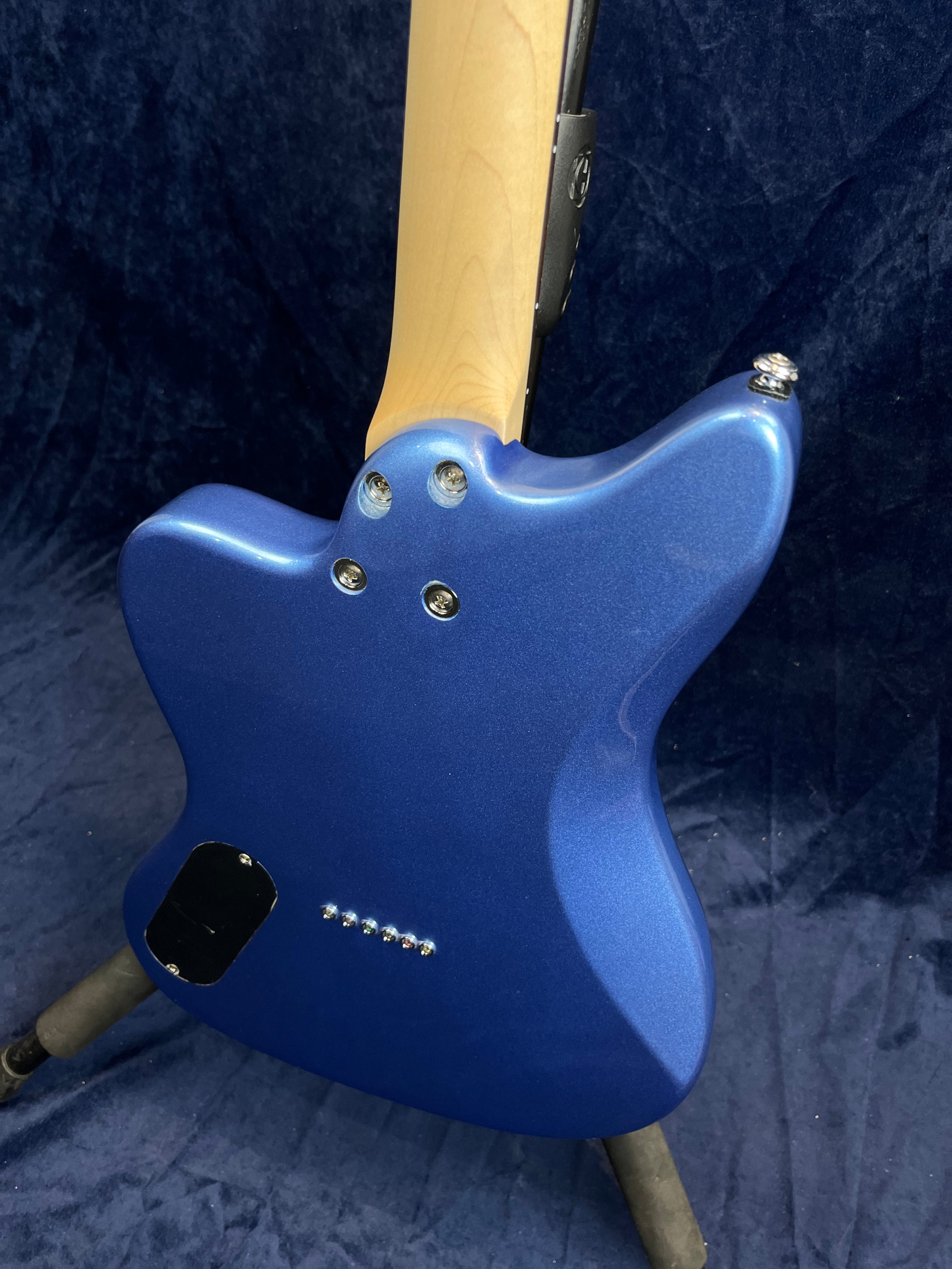 Metallic blue electric guitar shown from the back, revealing six string-through holes and a light wood neck attached with four bolts.