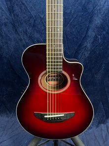Yamaha acoustic guitar with a glossy red sunburst body, six strings, cutaway design, and a circular sound hole bordered by concentric rings.
