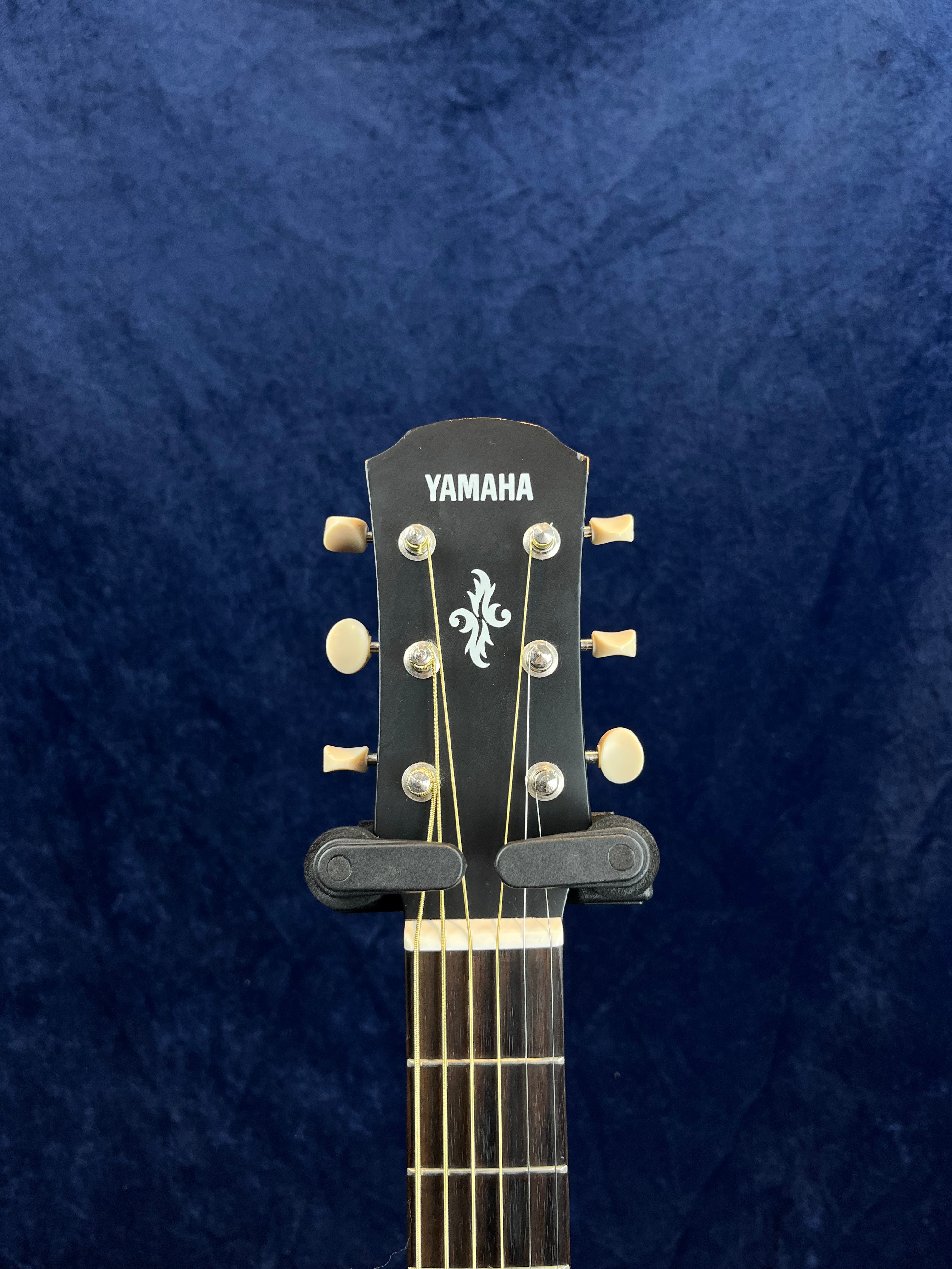 Yamaha acoustic guitar headstock with six tuning pegs, gold hardware, decorative inlay, and a capo clamped on the neck.