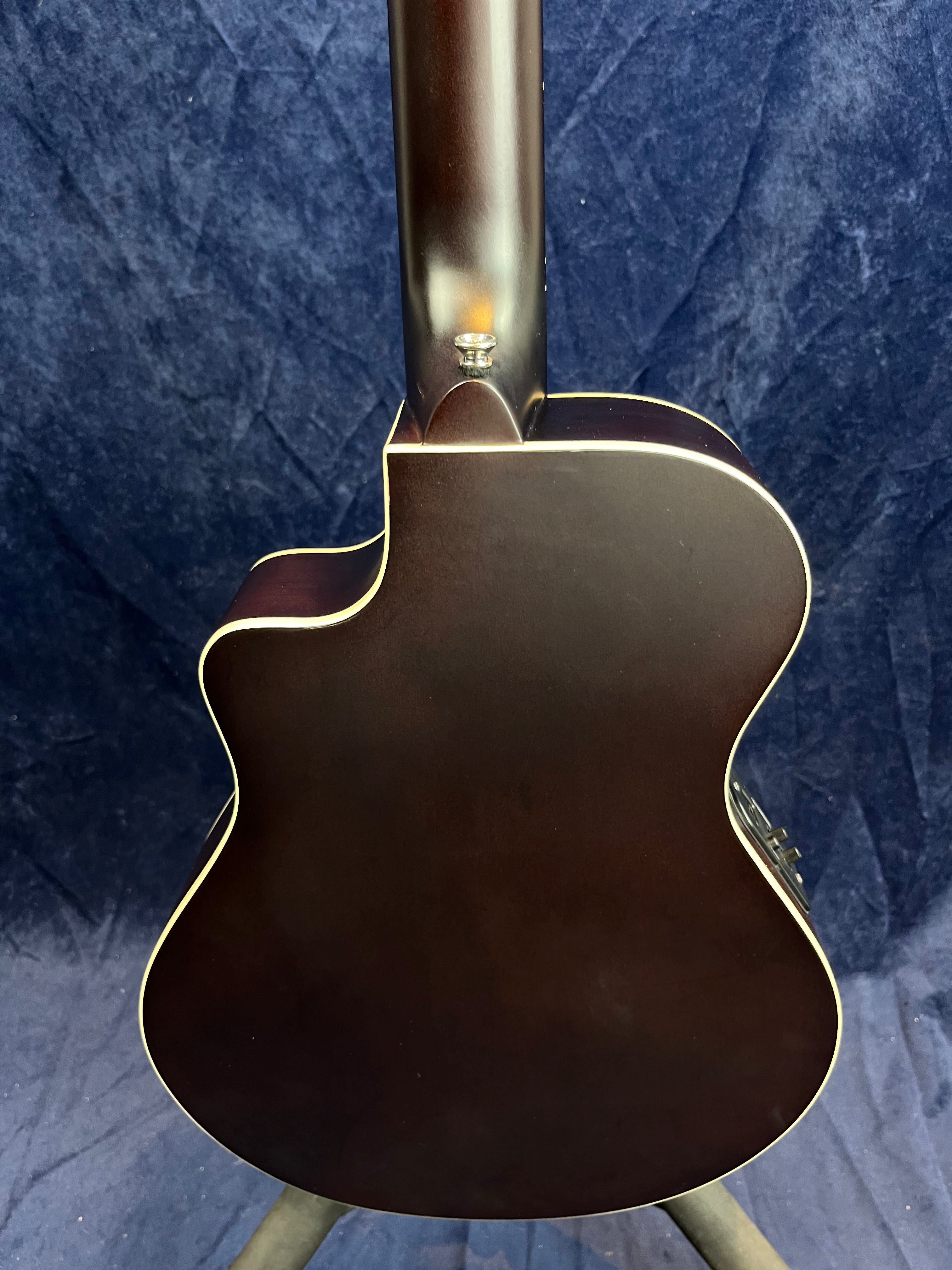 Dark brown acoustic guitar body seen from the back, featuring cream-colored binding along the edges and a cutaway design for easier upper fret access.