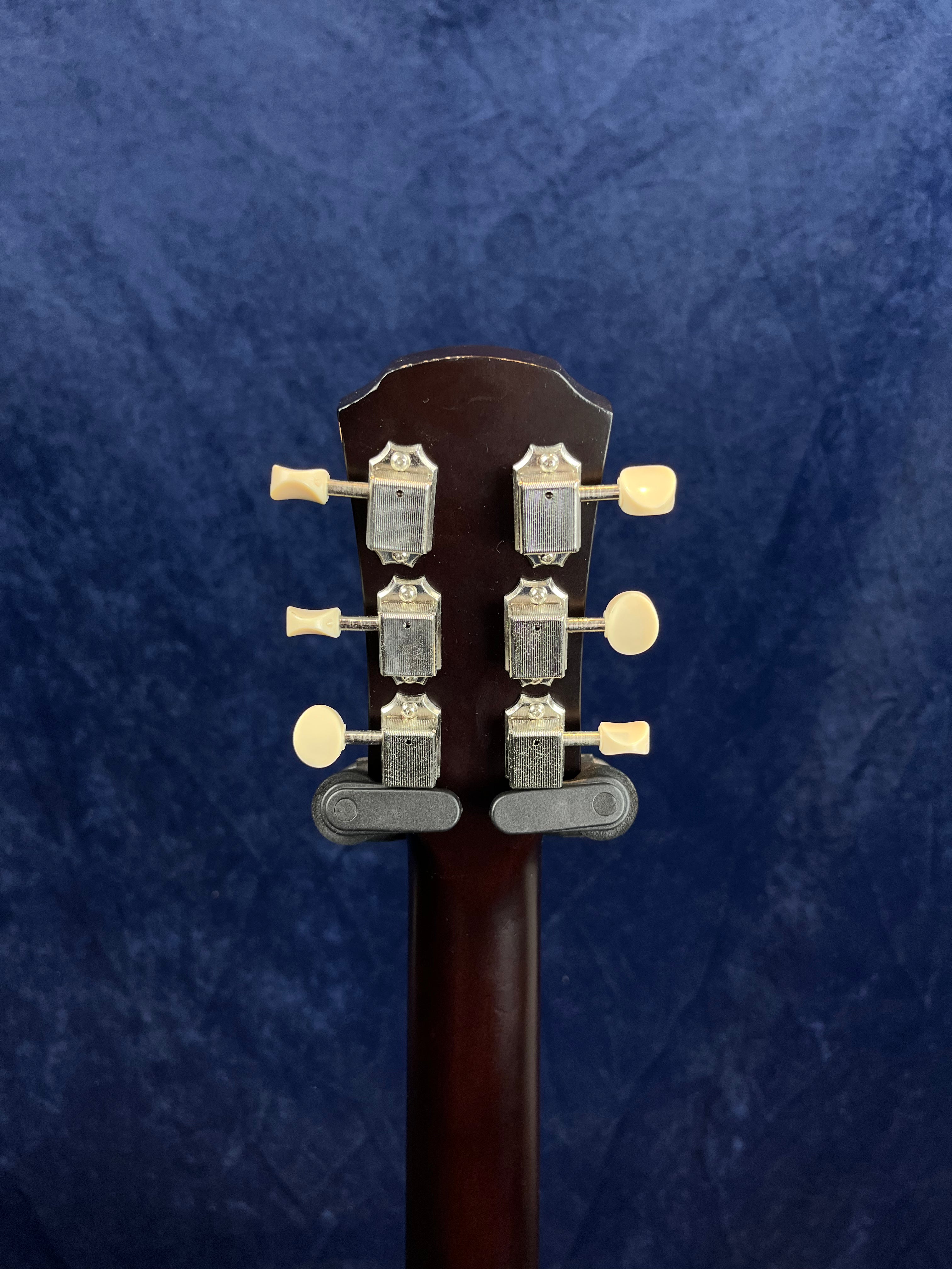 Six cream tuning pegs and silver machine heads on the dark wood headstock of an acoustic guitar, shown against a dark blue textured background.