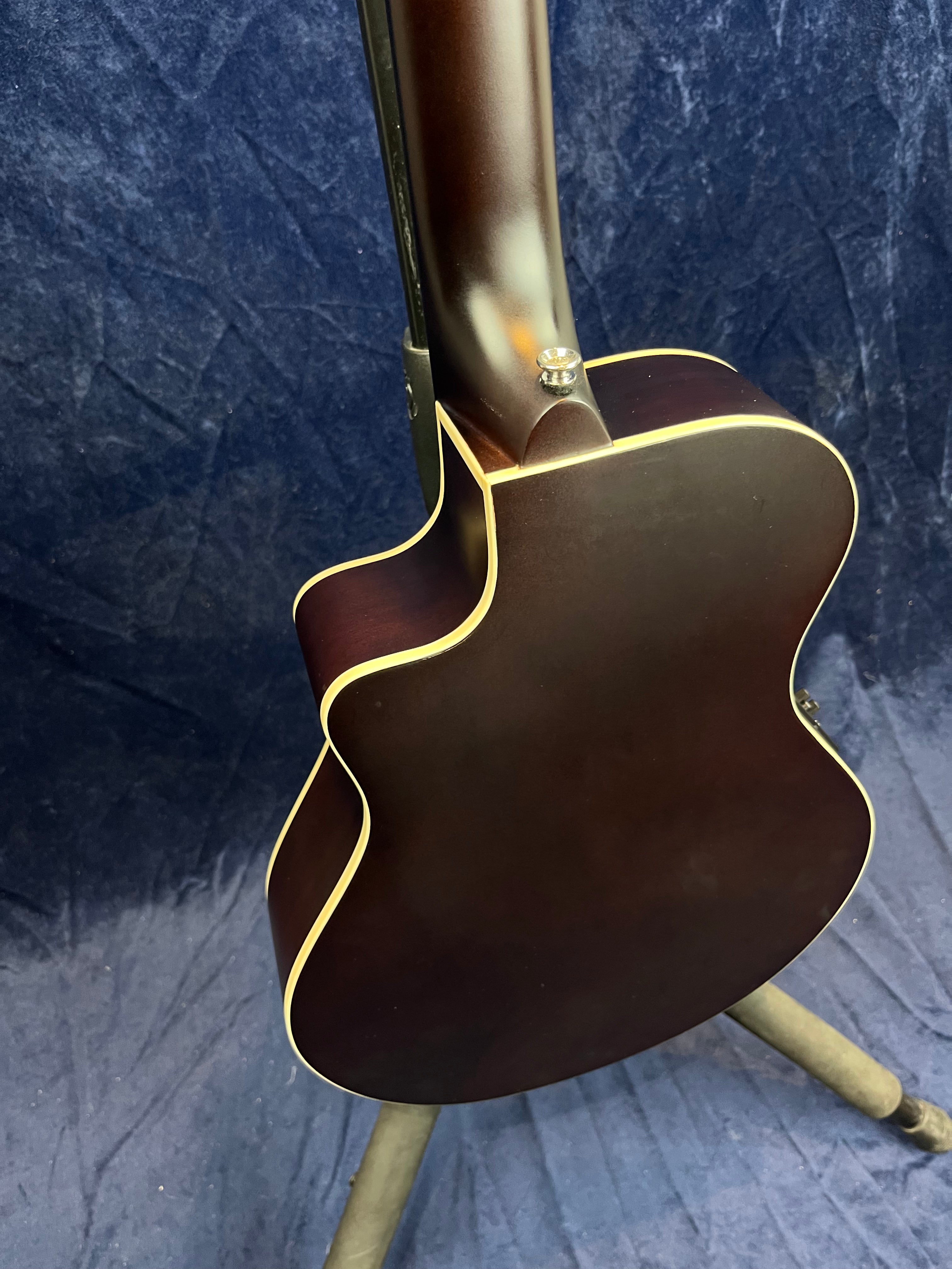 Dark brown acoustic guitar with cream binding, shown from the back. The body has a single cutaway and a satin finish.
