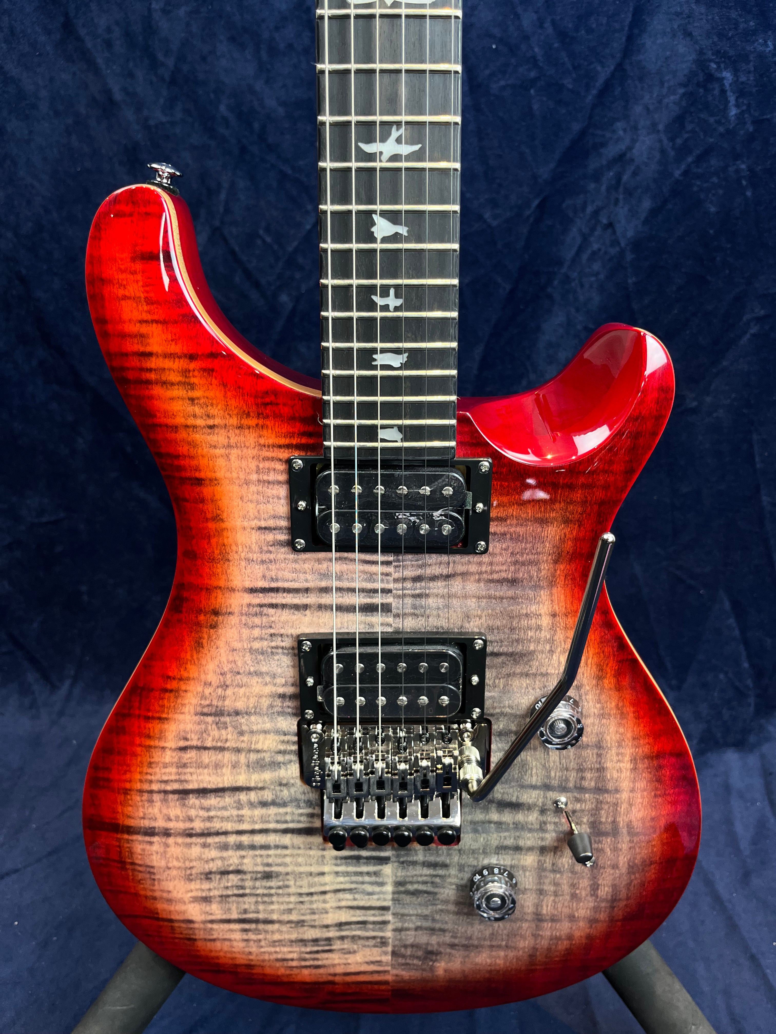 Electric guitar with a red sunburst finish, two humbucker pickups, tremolo bridge, and fretboard inlays shaped like birds.