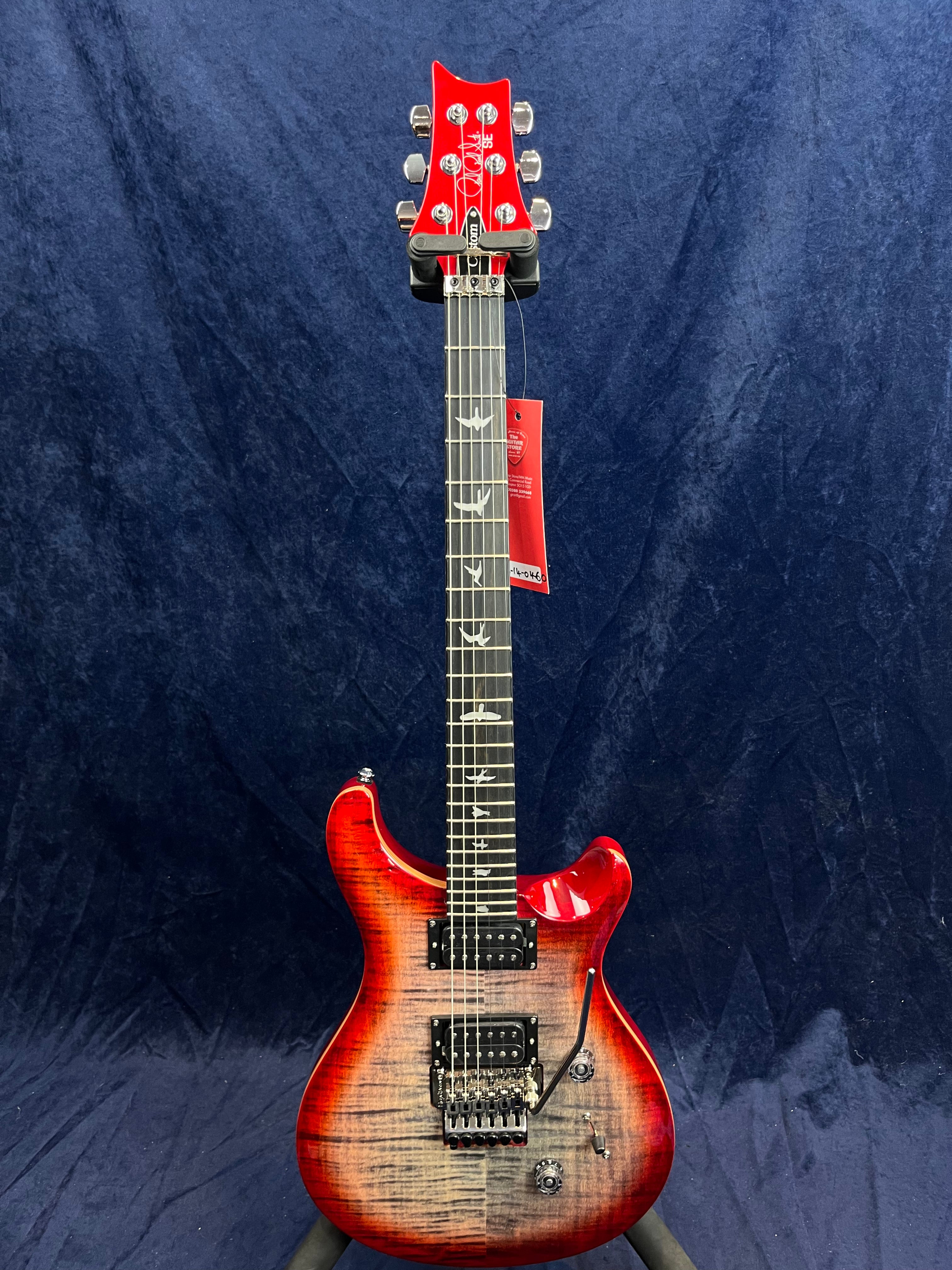 Red and black electric guitar with bird inlays on the neck, two humbucker pickups, and a whammy bar against a dark blue background.
