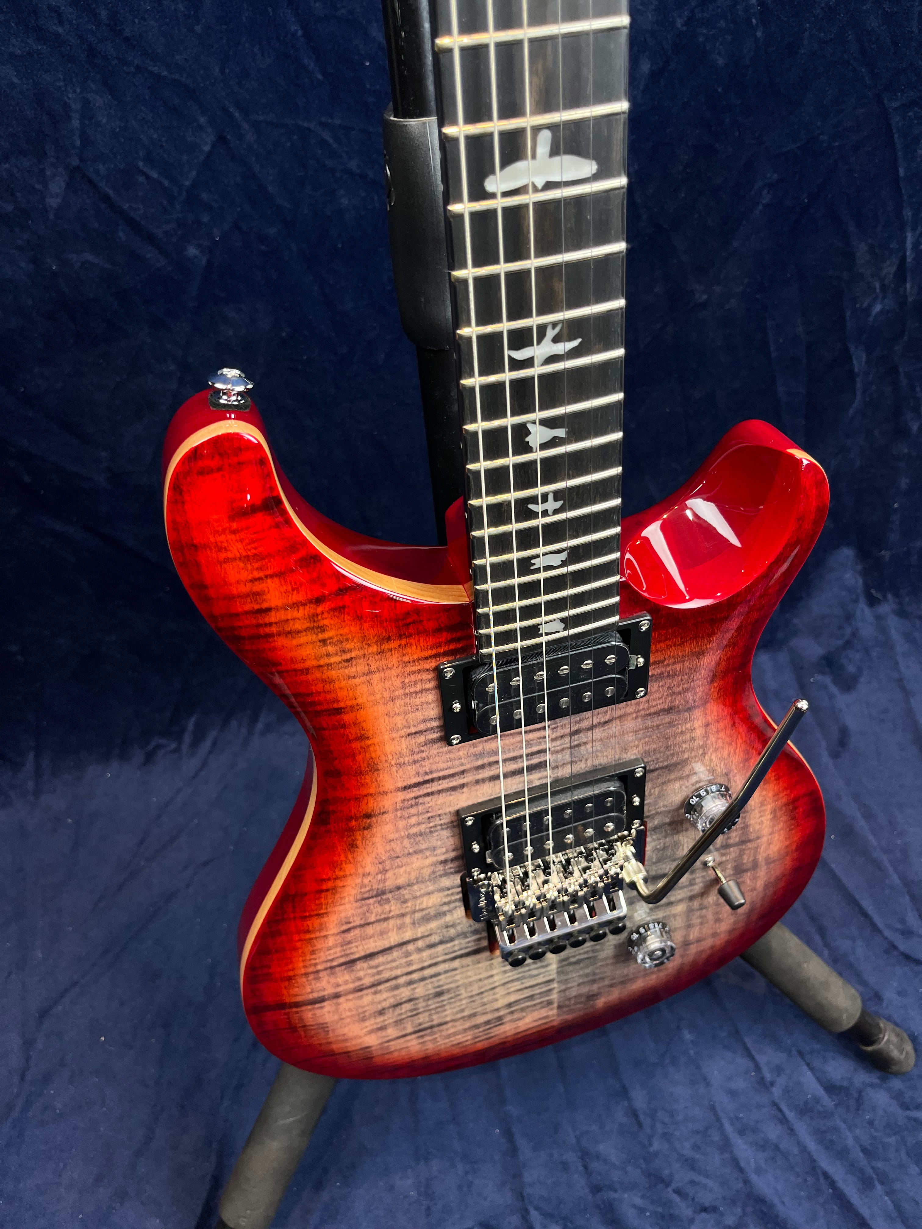 Red electric guitar with a flamed maple top, double humbucker pickups, a tremolo bridge, and bird-shaped inlays on the fretboard.