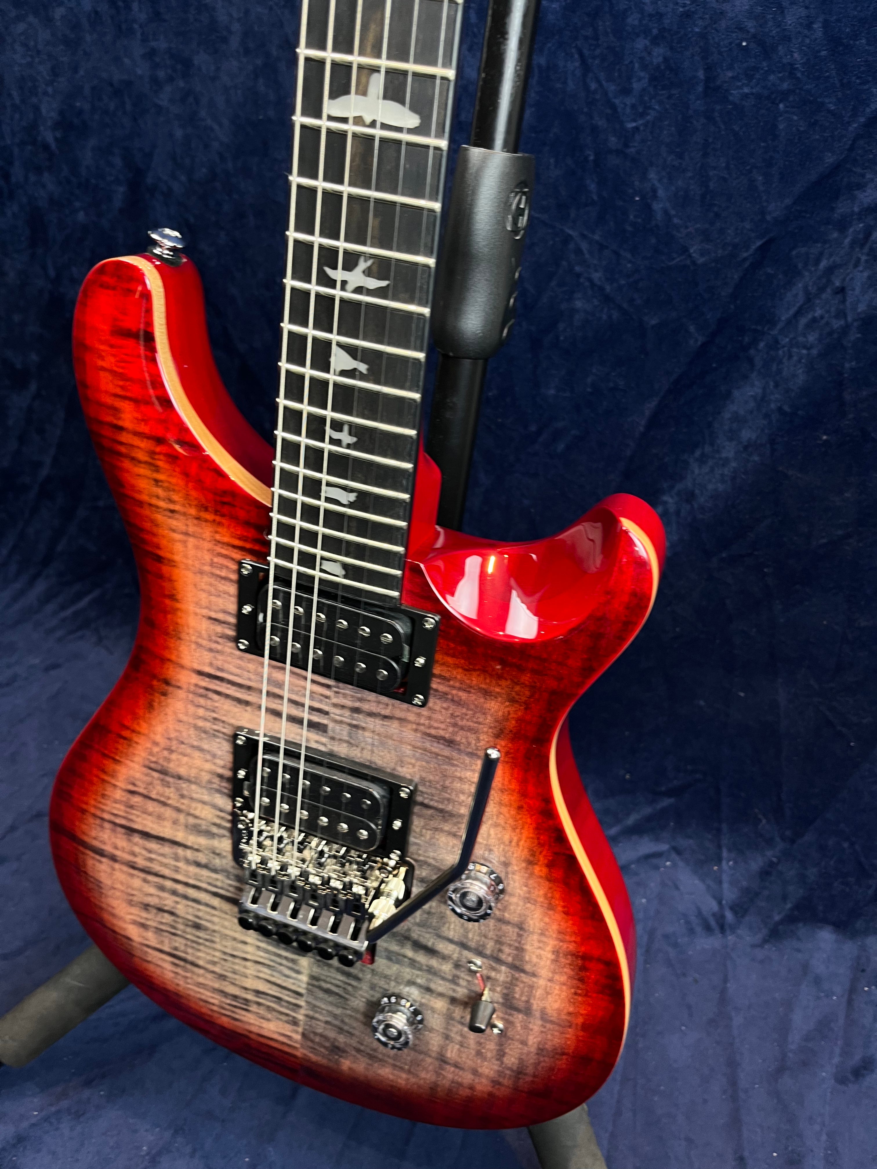 Red and black electric guitar with a flamed wood finish, two humbucker pickups, a whammy bar, and bird inlays on the fretboard.
