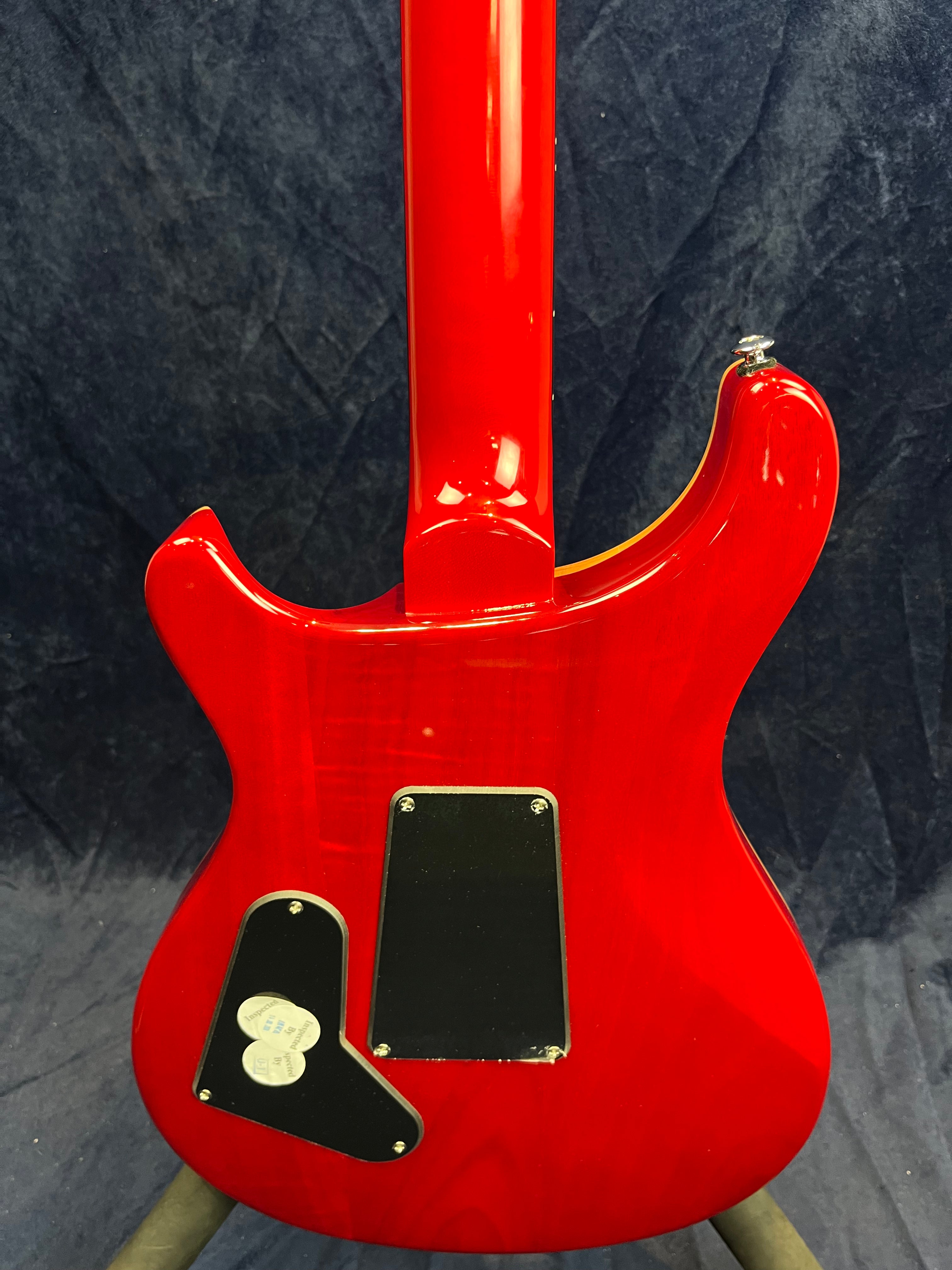 Bright red electric guitar back with two black plastic access covers and visible neck joint, set against a dark textured background.