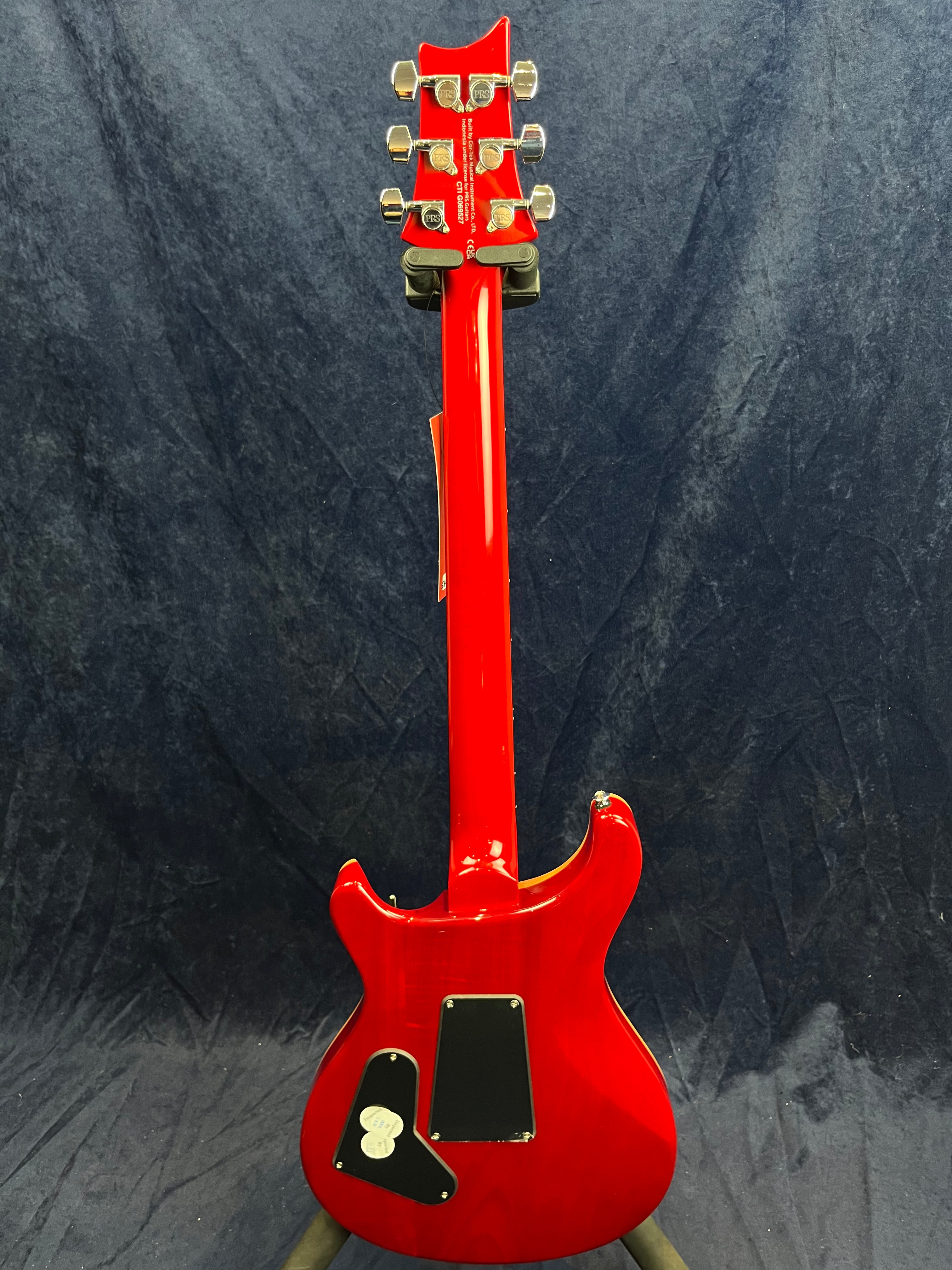 Red electric guitar shown from the back, displaying chrome tuning pegs, two black plastic cover plates on the body, and a glossy finish.