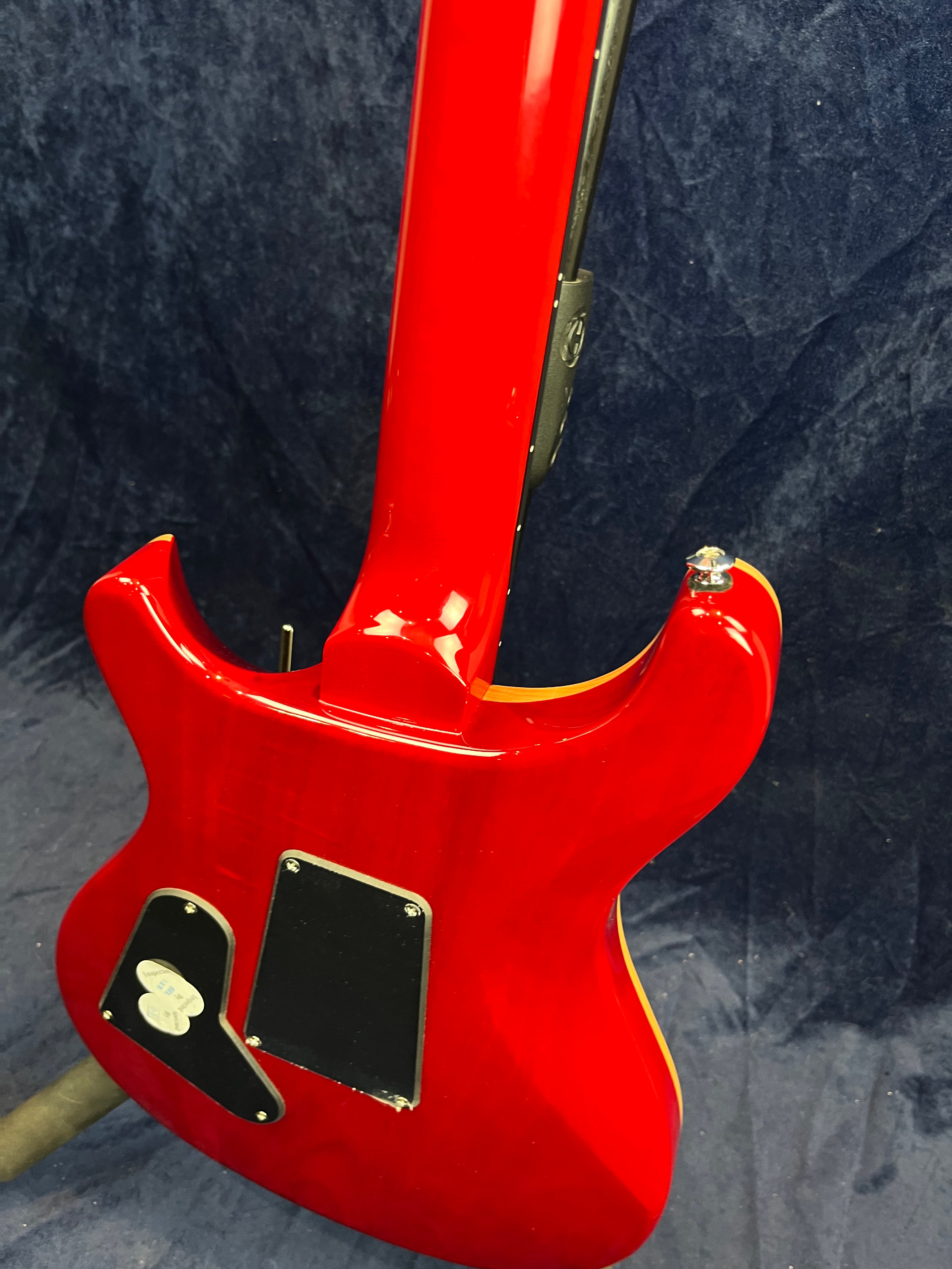 Glossy red electric guitar back with two black control cavity covers and visible wood grain, set against a dark blue background.