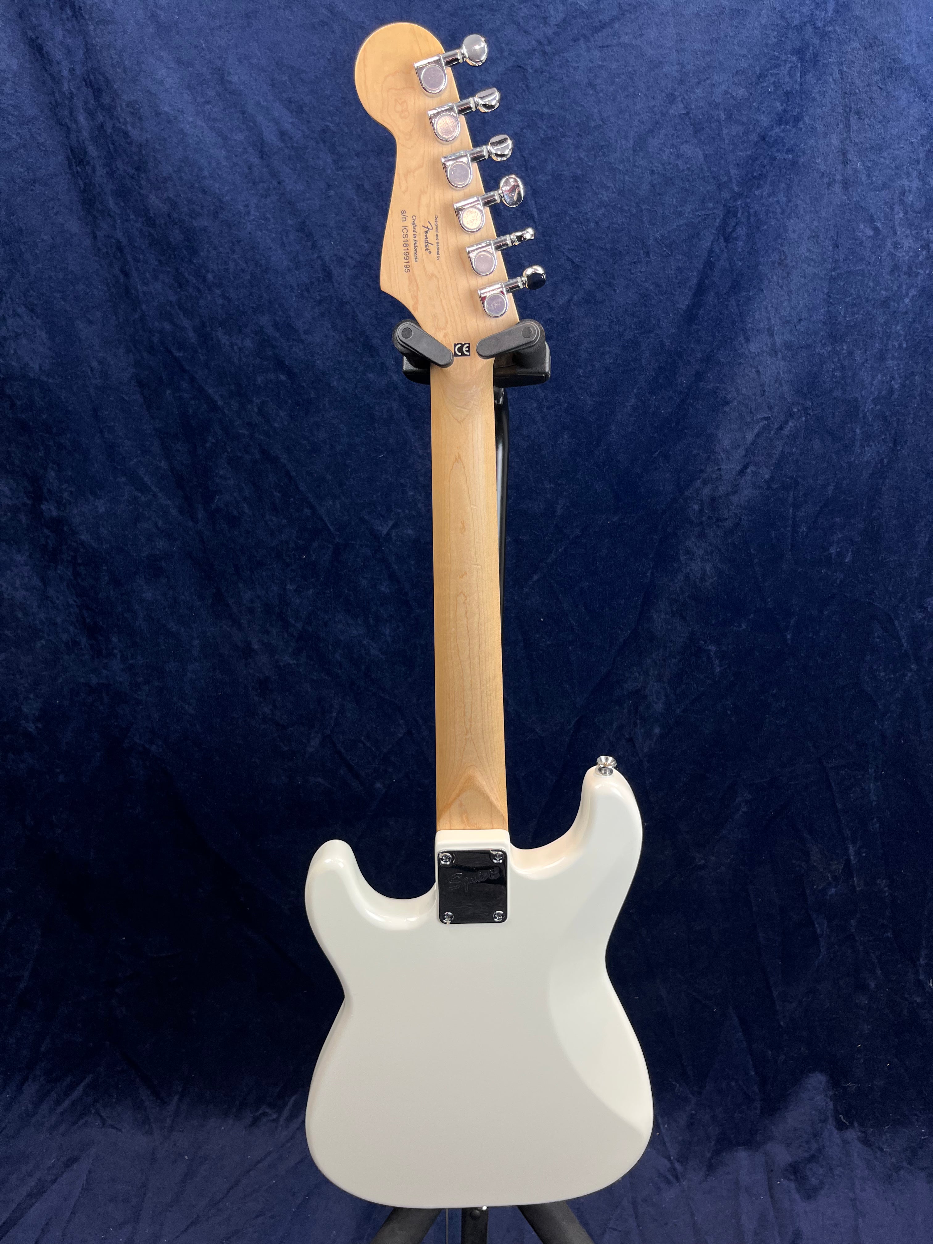 White electric guitar shown from the back, displaying a light wood neck with six tuning pegs and a contoured body against a dark blue background.