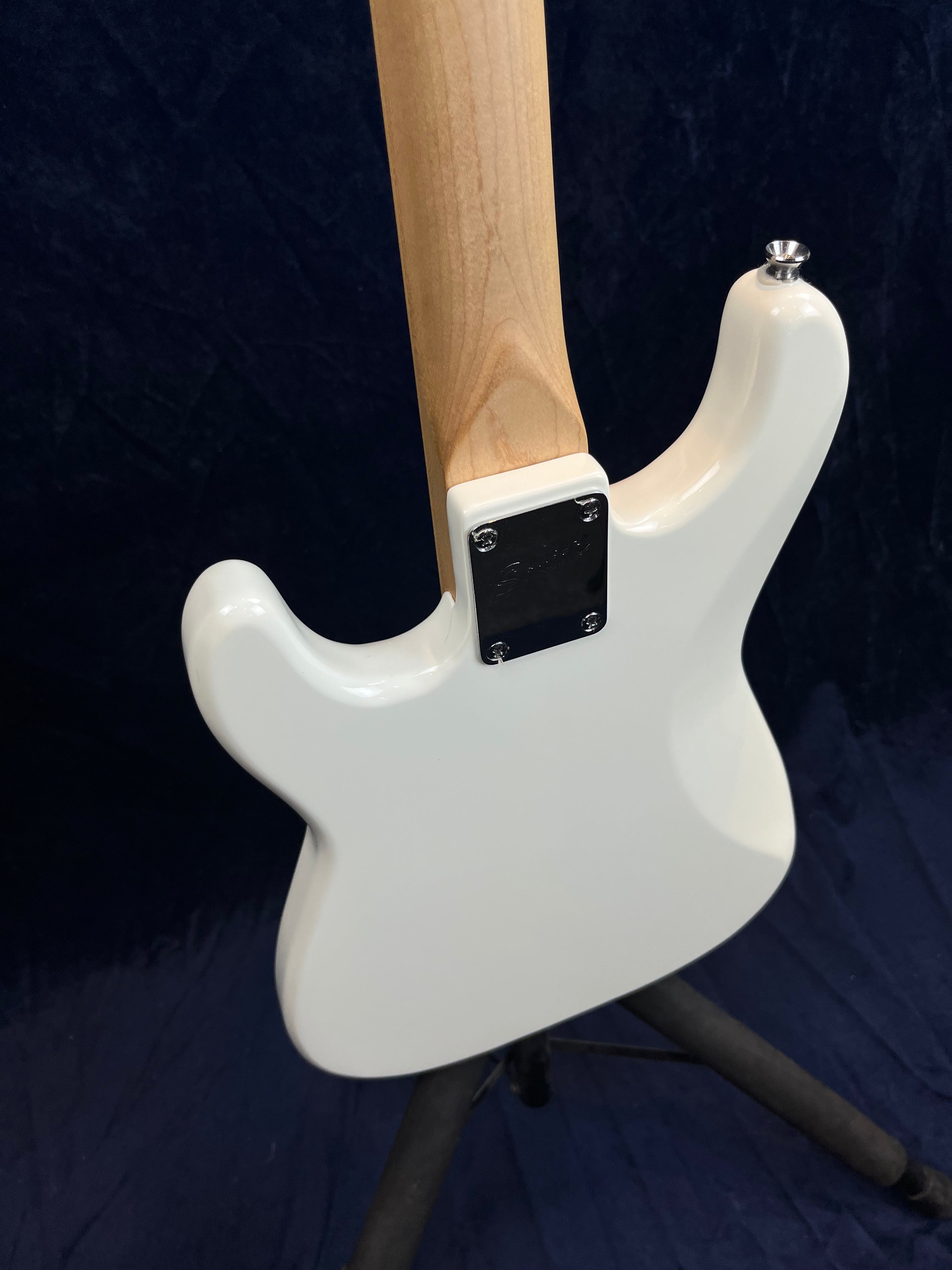 Back view of a white electric guitar showing the neck joint with a metal plate and the upper part of the body resting on a stand.