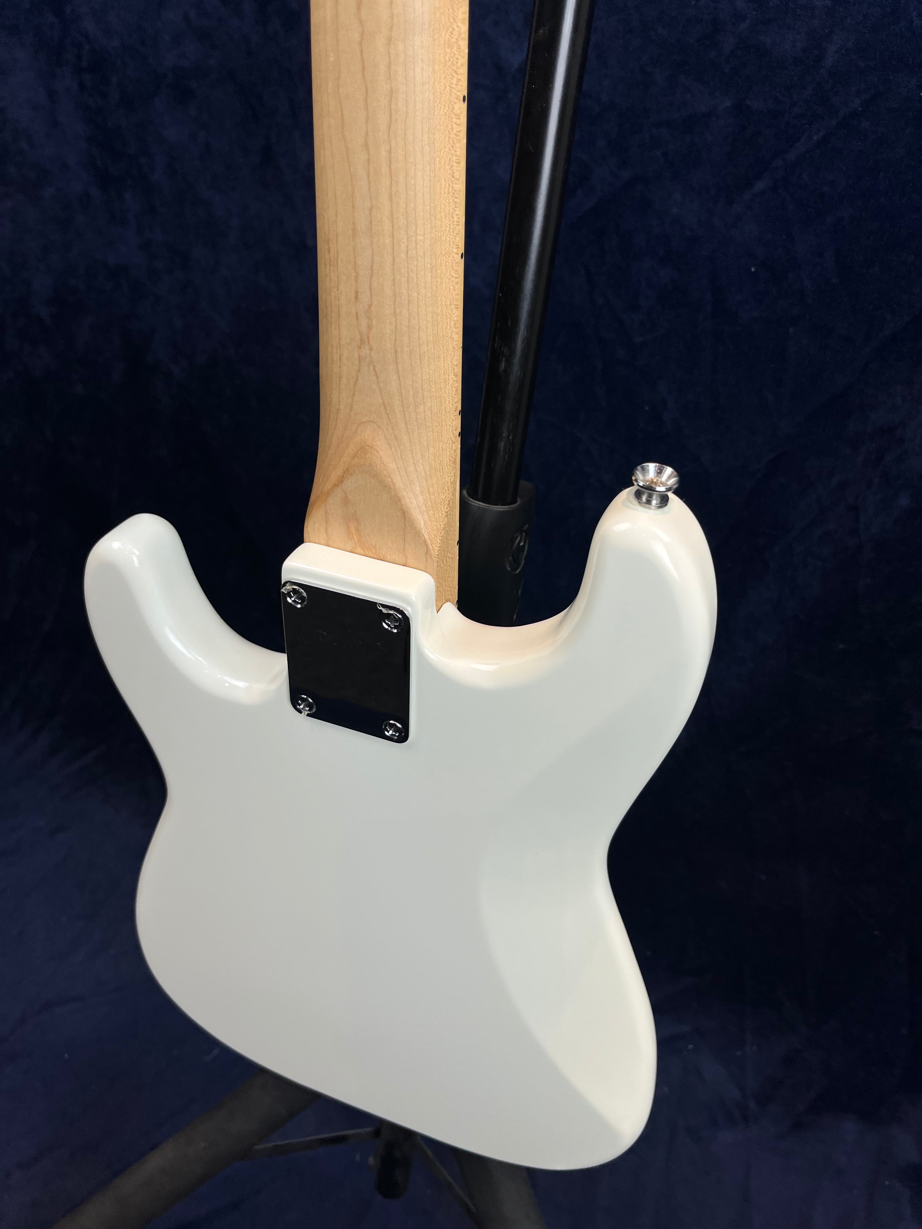 White electric guitar rear view showing glossy body, bolt-on natural wood neck with a metal plate, and a strap button on the upper horn.