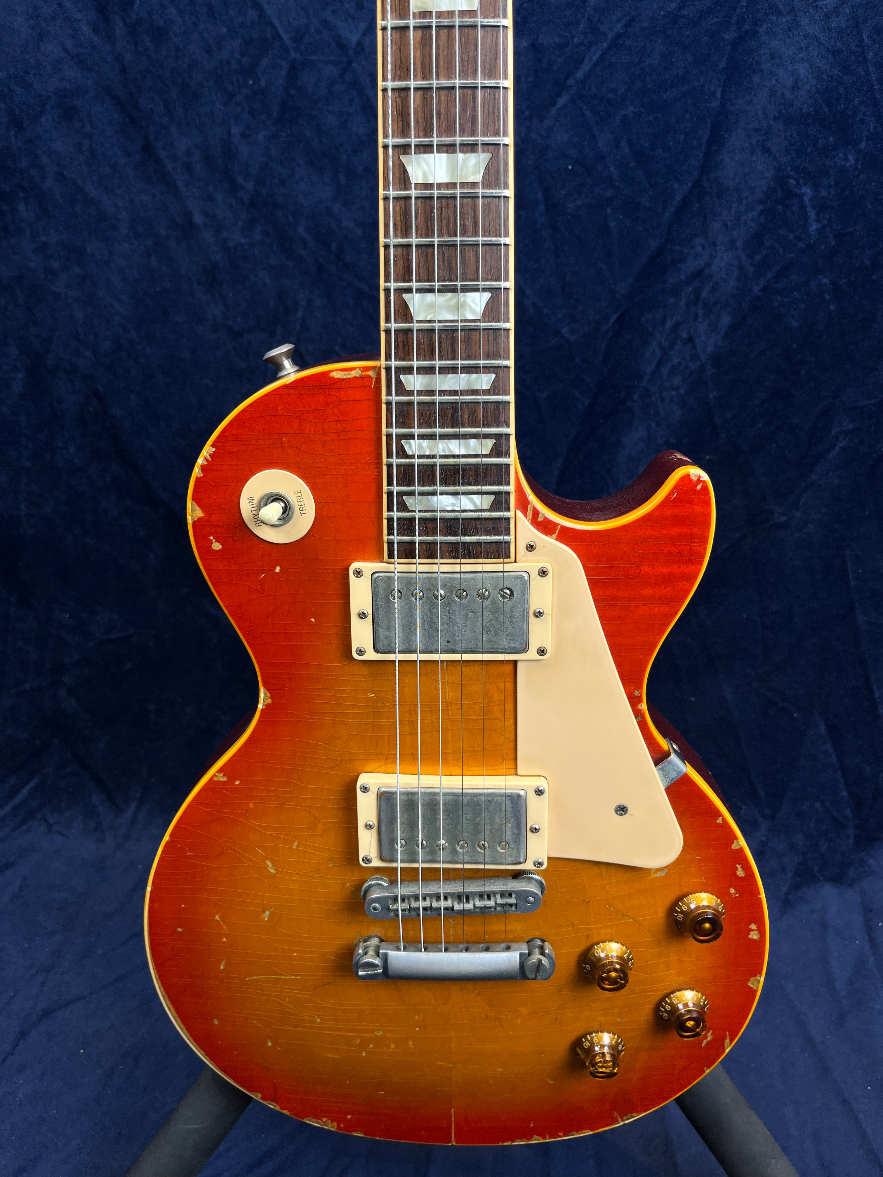 Sunburst electric guitar with a single cutaway, two humbucker pickups, cream pickguard, and visible wear and scratches on the body.