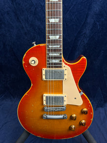 Sunburst electric guitar with a single cutaway, two humbucker pickups, cream pickguard, and visible wear and scratches on the body.