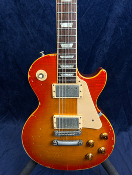 Sunburst electric guitar with a single cutaway, two humbucker pickups, cream pickguard, and visible wear and scratches on the body.