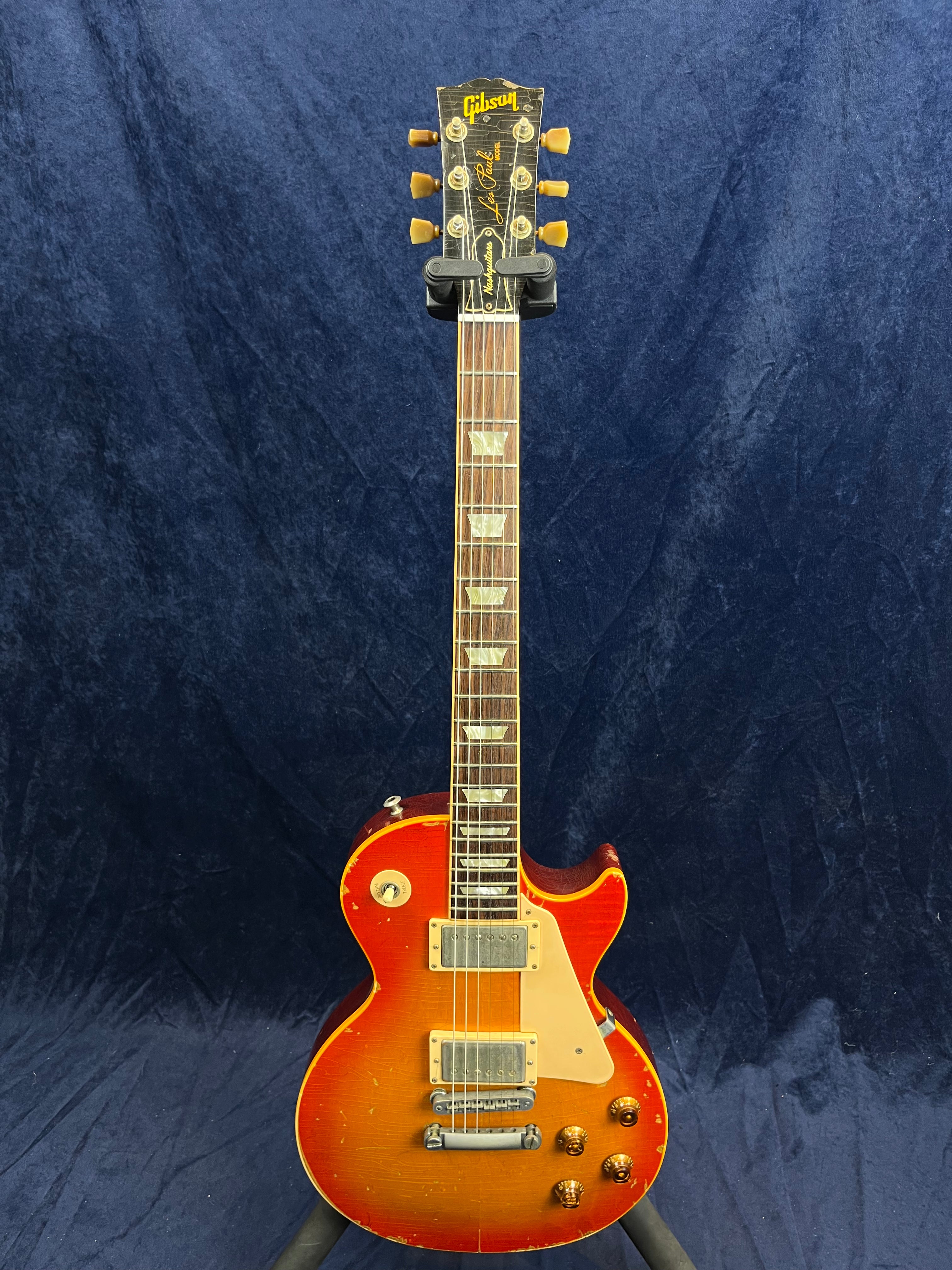 Sunburst-finish Gibson Les Paul electric guitar with two humbucker pickups, four control knobs, and a cream pickguard, showing visible wear.