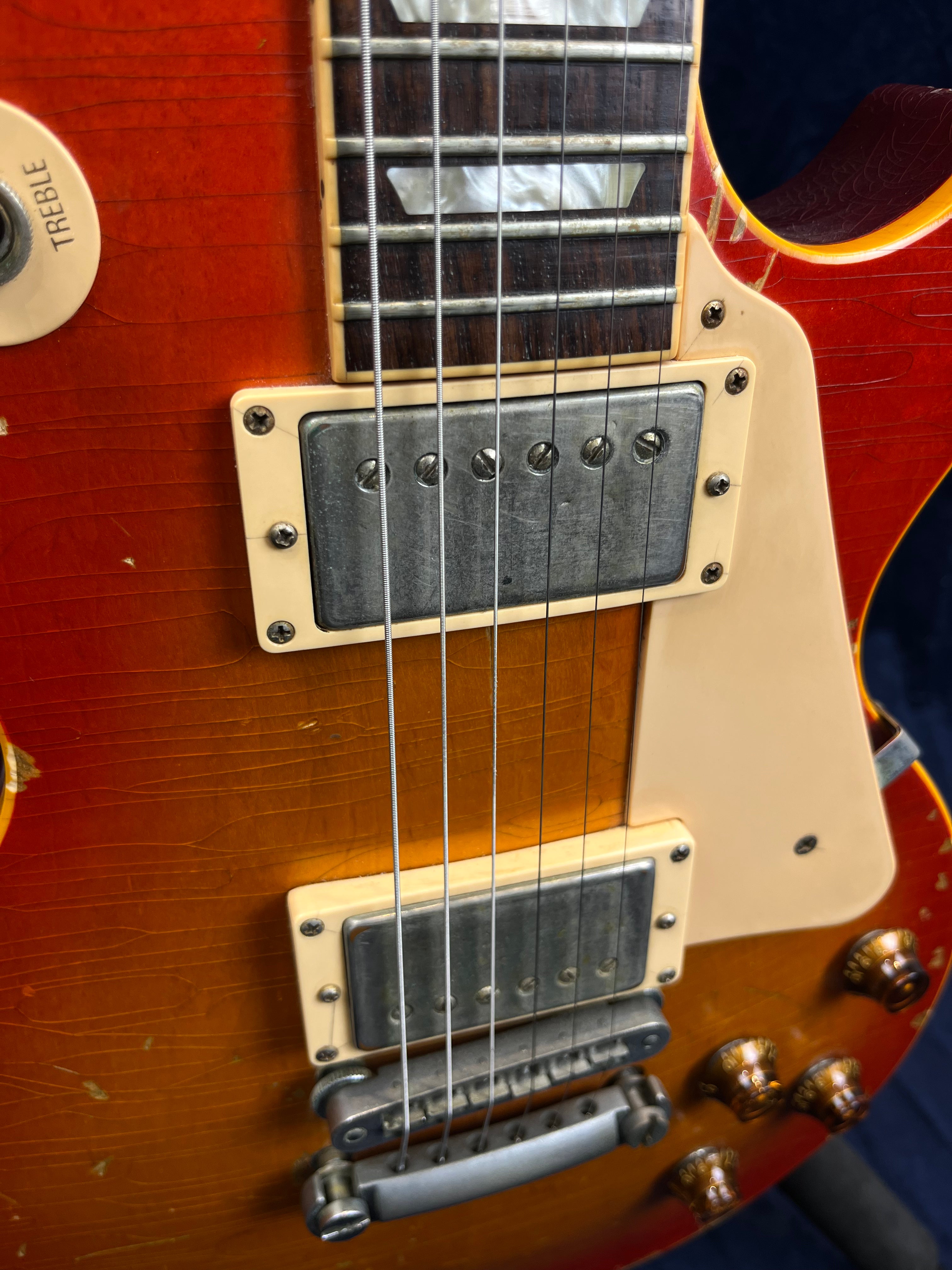 Close-up of an electric guitar showing strings, two silver humbucker pickups, amber knobs, and a sunburst finish with visible wood grain cracks.