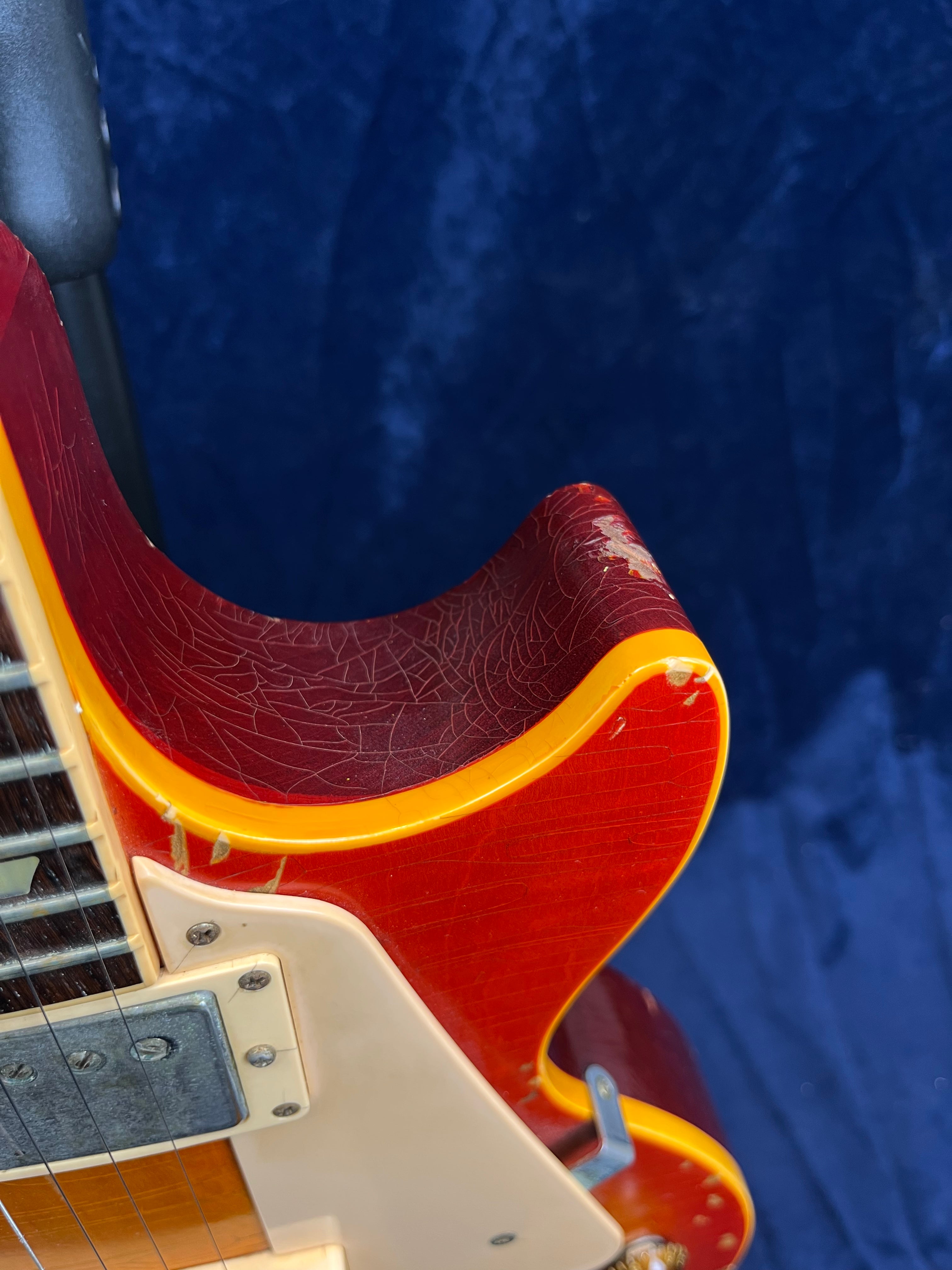 Upper body of a red electric guitar with yellow edges, showing cracked and worn finish near the curve and slight chipping of the paint.