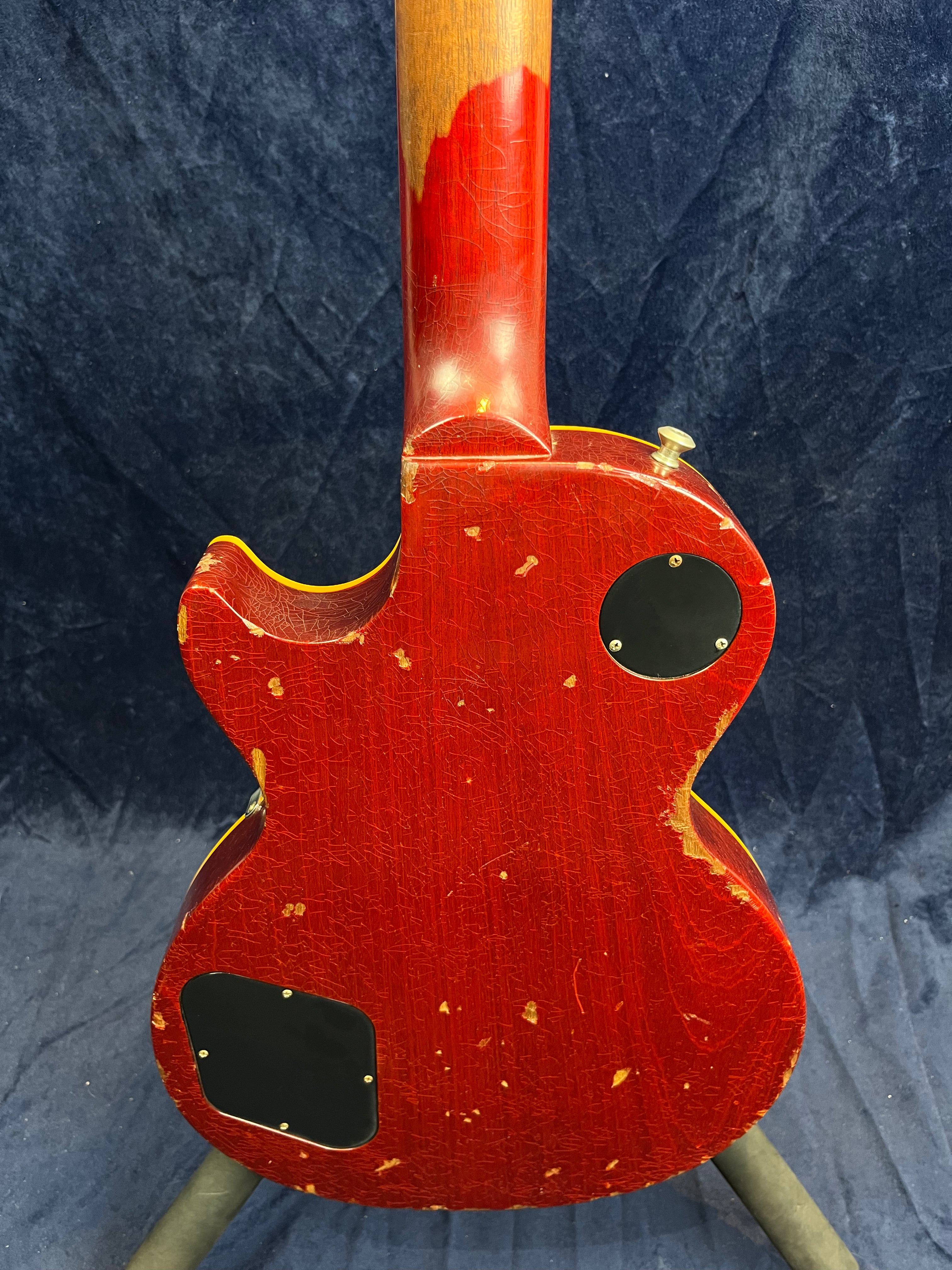 Back of a red electric guitar with heavy wear, wood showing through on the neck and edges, and two black control cavity covers.