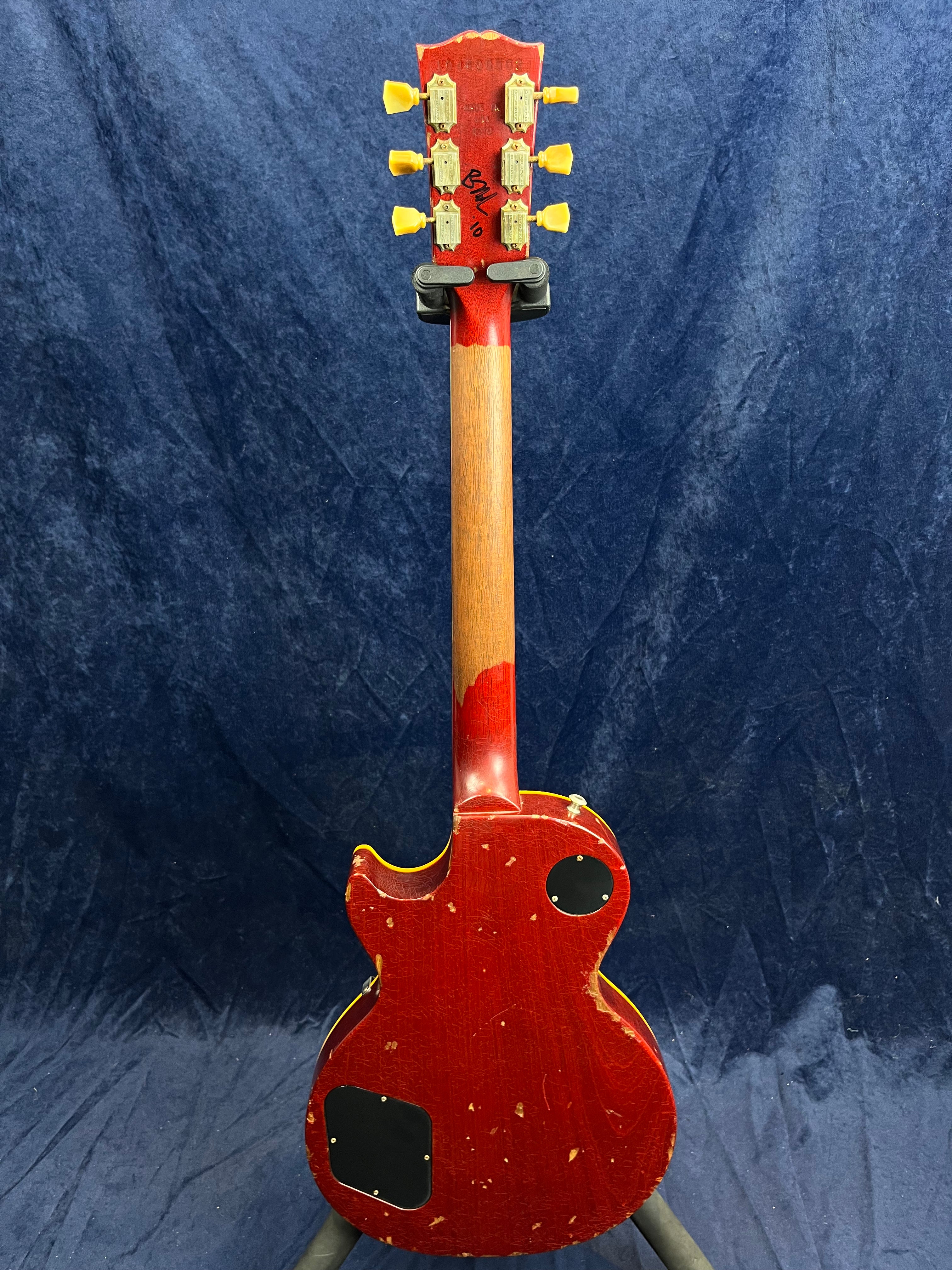 A red electric guitar seen from the back, showing worn paint, two black control cavity covers, yellow tuner knobs, and a partially faded neck finish.