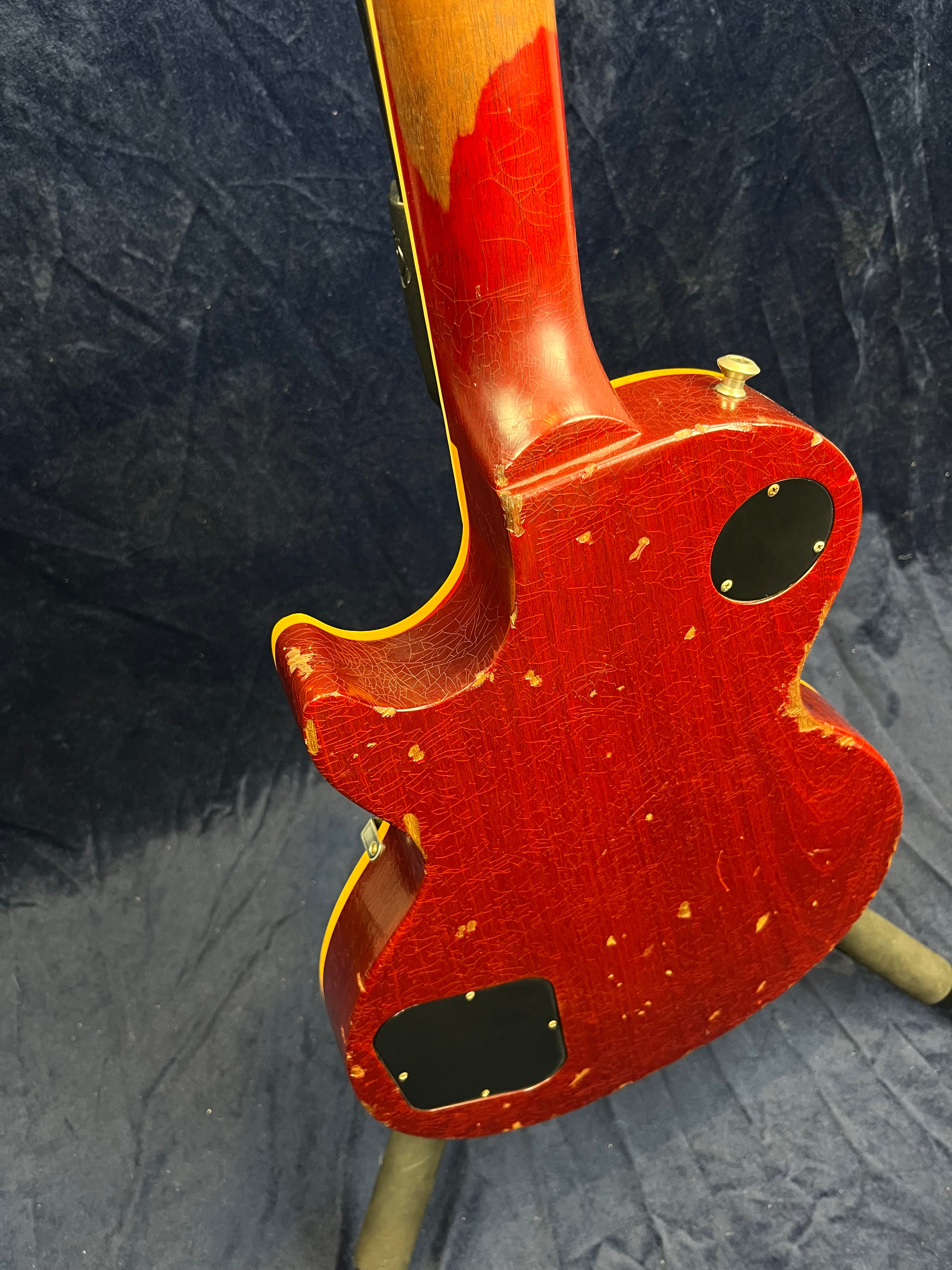 Red electric guitar with heavy finish wear and paint chips exposing wood, yellow edging, visible neck wear, and two black control cavity covers on the back.