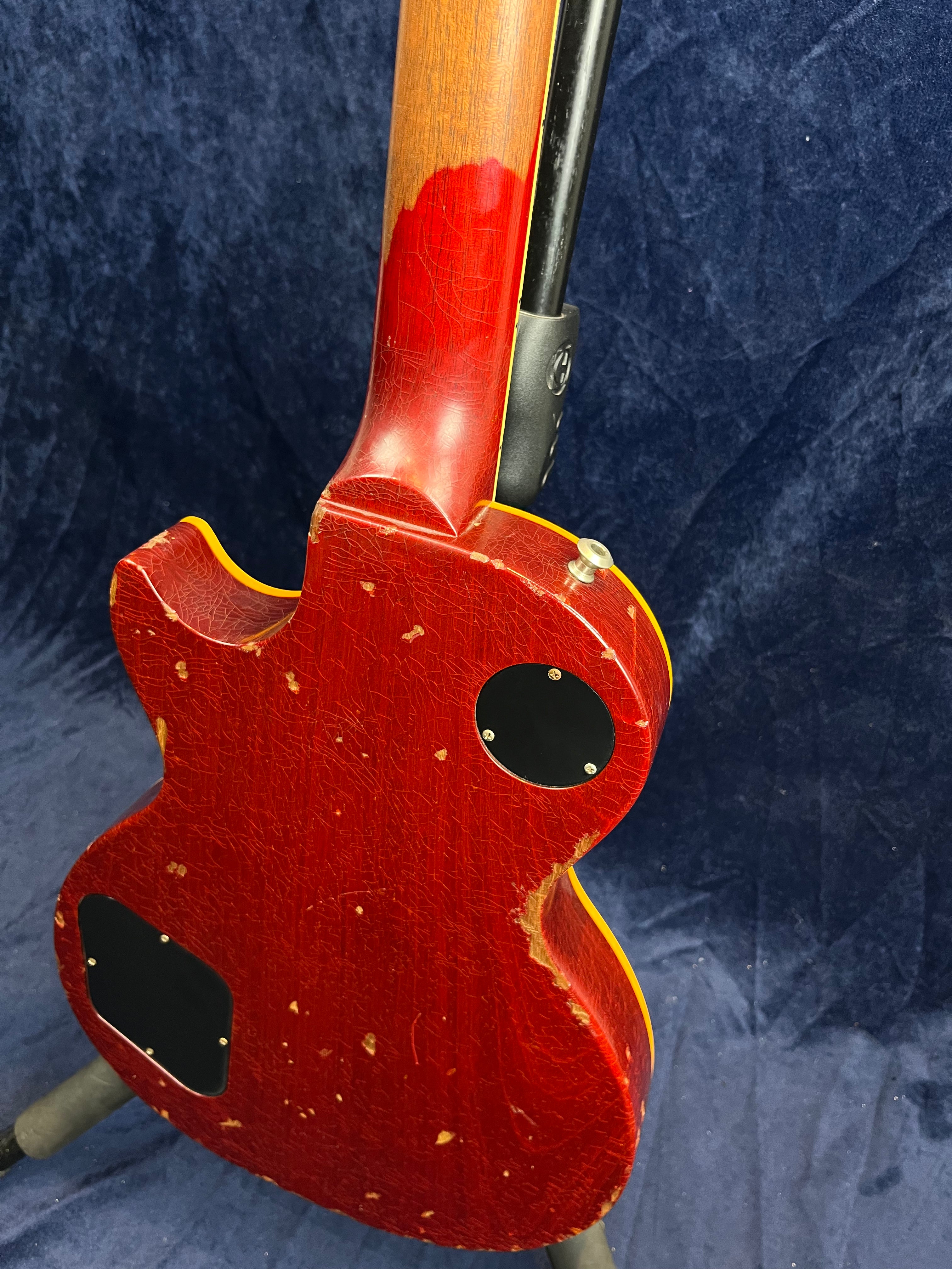 Red electric guitar with heavy wear, chipped edges, visible wood on the neck, and black plastic control cavity covers on the back.