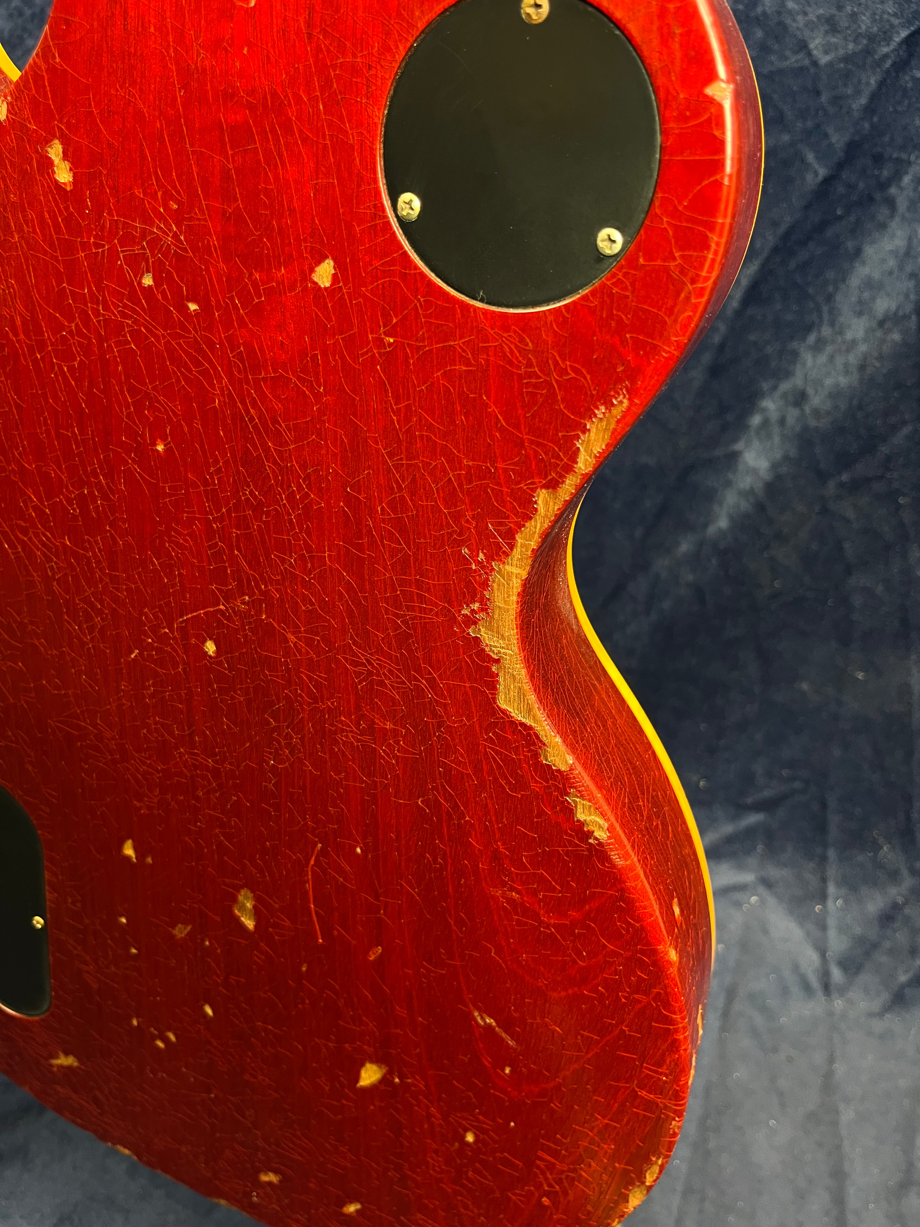 Red electric guitar back with heavy finish wear, scratches, and chips revealing wood, plus a black round cavity cover with four screws.