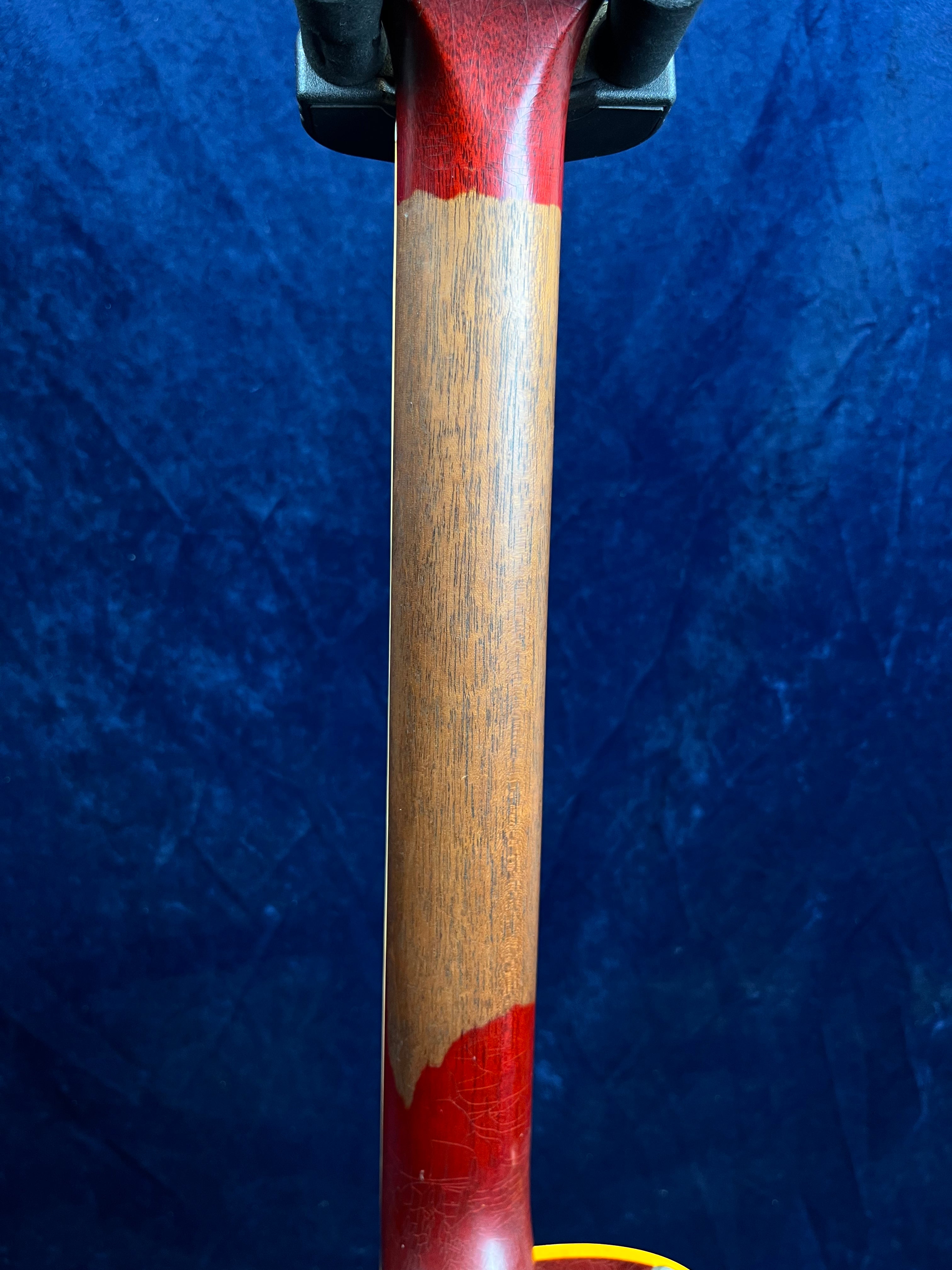 Electric guitar neck showing worn wood in the middle section with red finish remaining at both ends against a dark blue background.