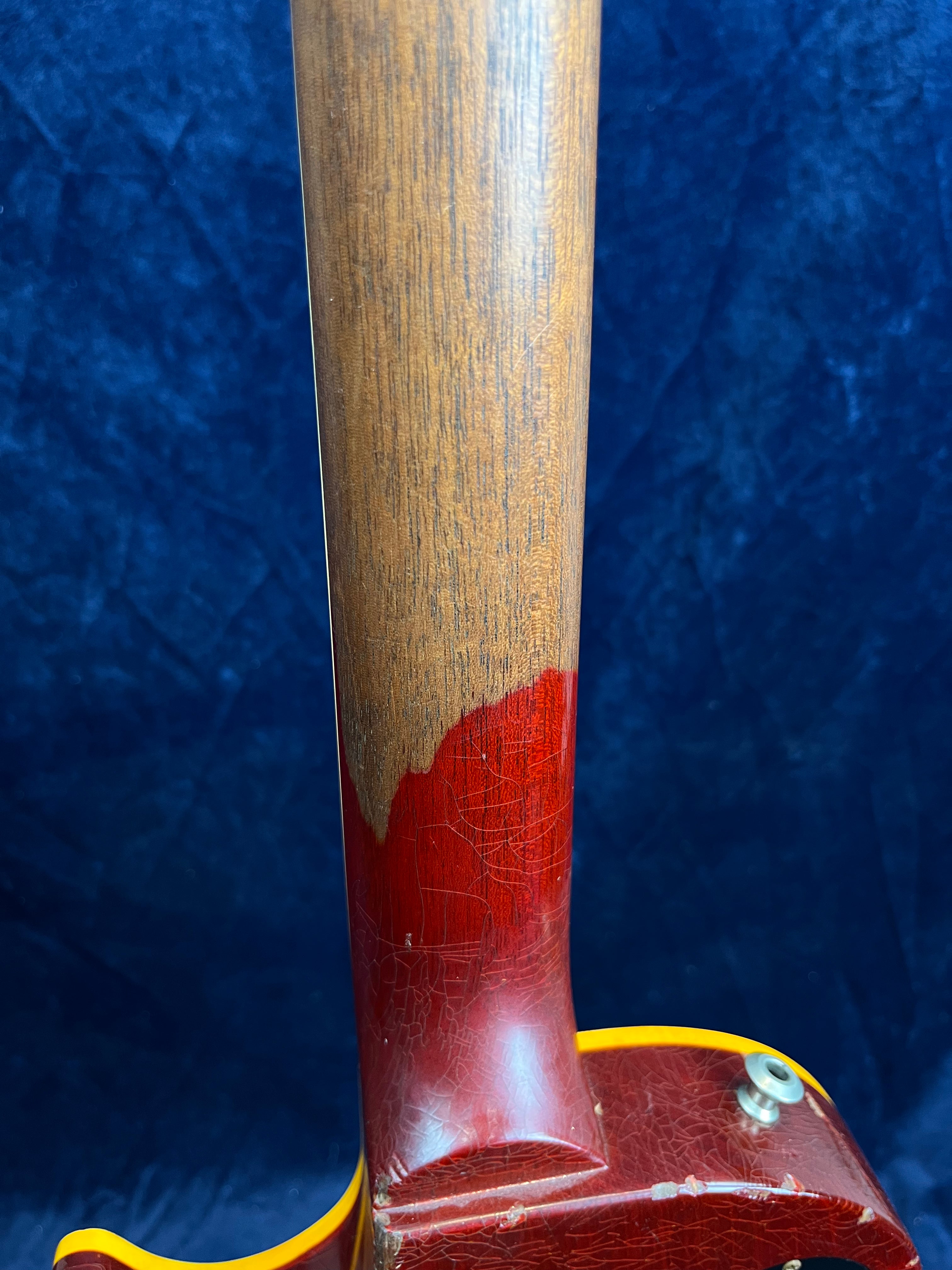 Electric guitar neck with worn reddish finish revealing natural wood, attached to a reddish body with yellow trim and visible aging cracks.