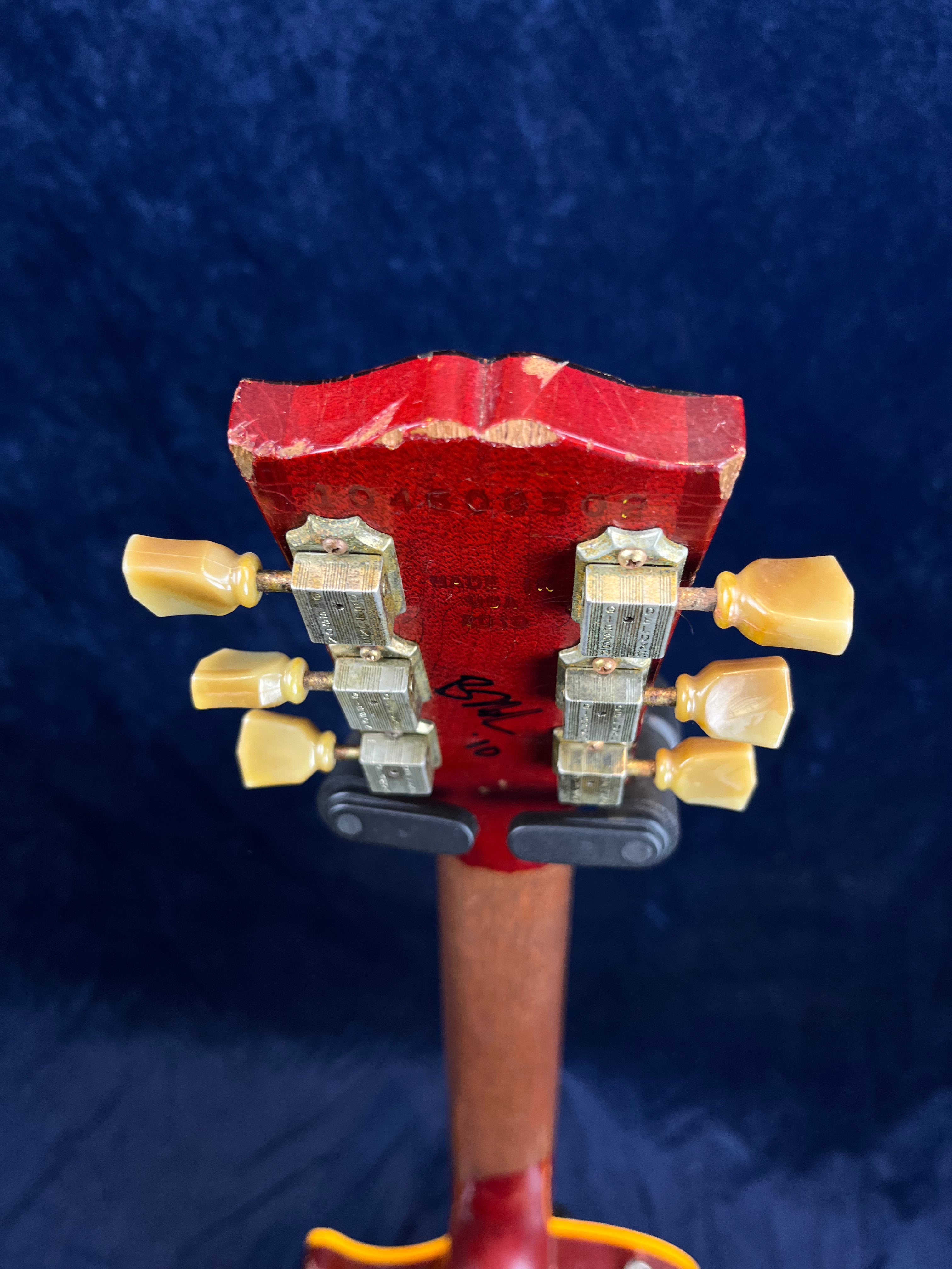 Red electric guitar headstock with six vintage-style tuners, cream tuning pegs, visible serial number, and signs of edge wear on the wood.